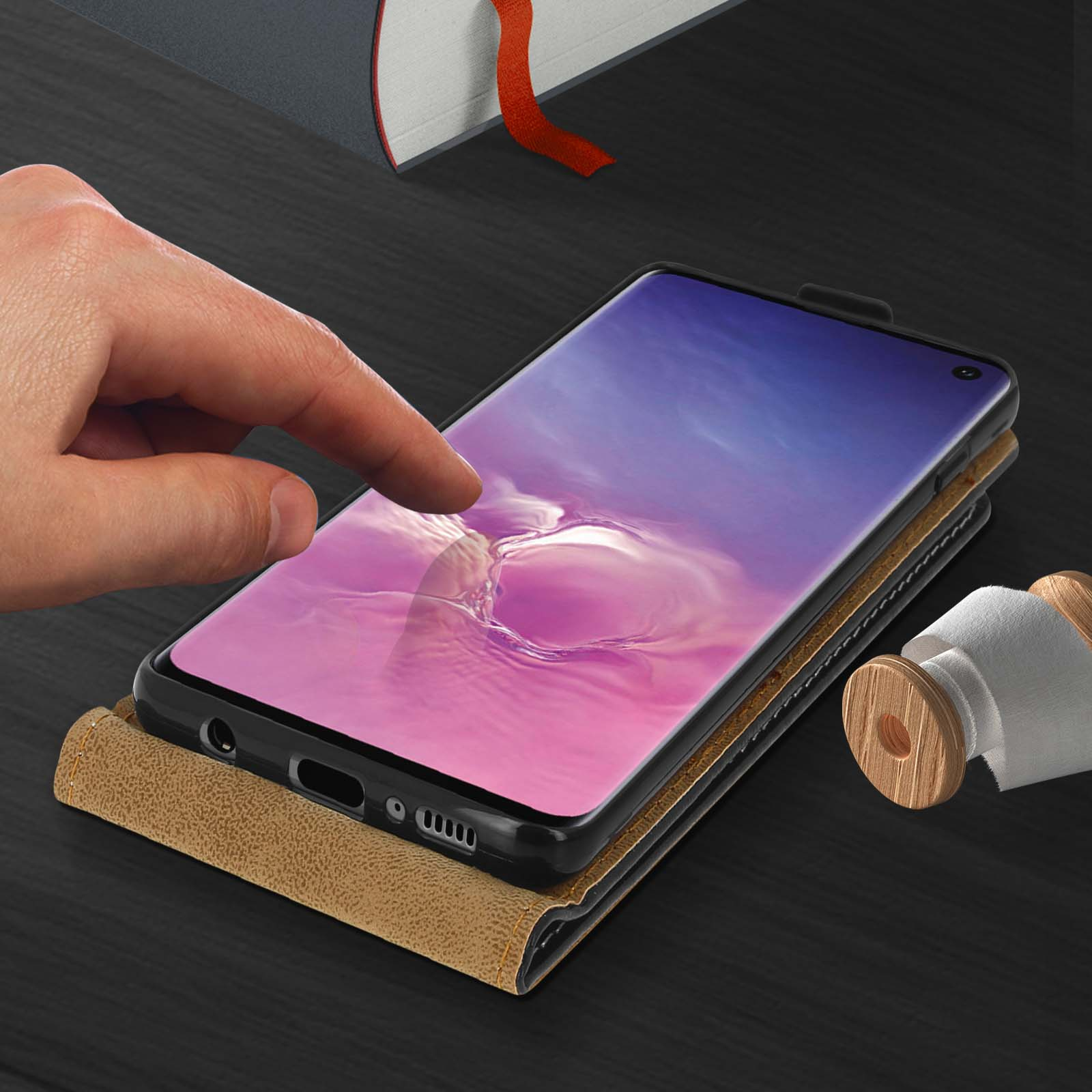 Eine Hand berührt den Telefonbildschirm. Das Smartphone liegt auf einem Tisch, im Hintergrund ein Buch.