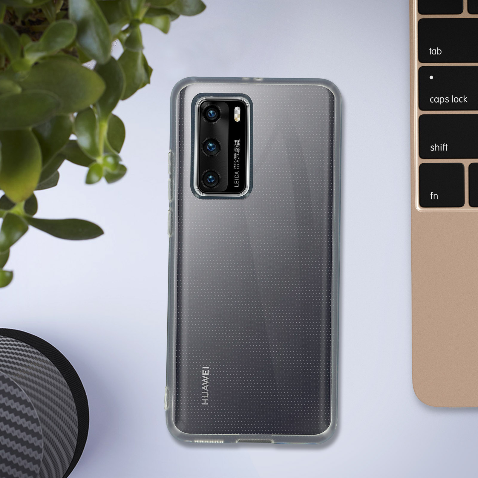 Téléphone avec une coque transparente sur une table, à côté d'une plante et d'un clavier.