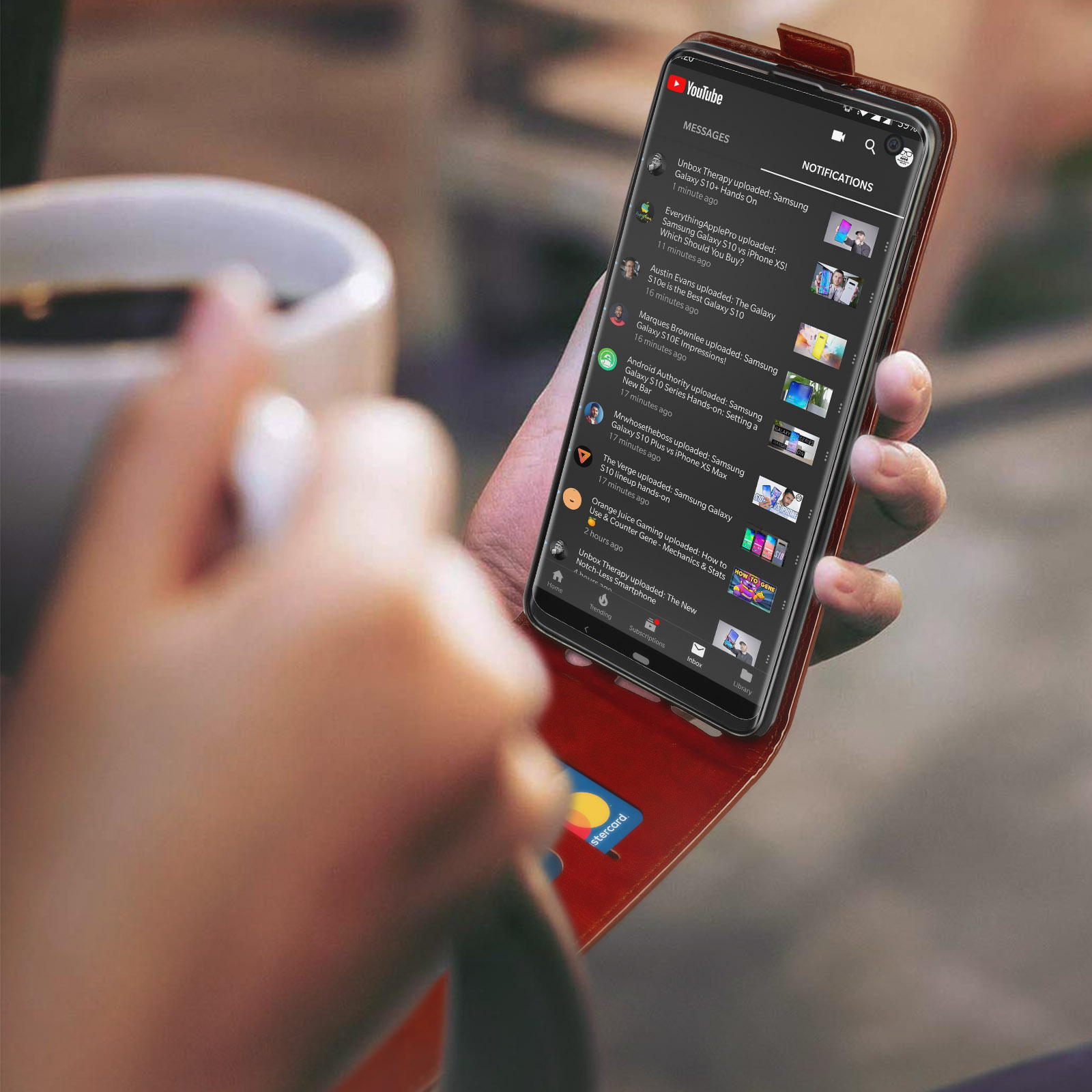 Un telefono con una custodia rossa, che mostra un video di YouTube. Una mano tiene il telefono e una carta di credito è visibile.