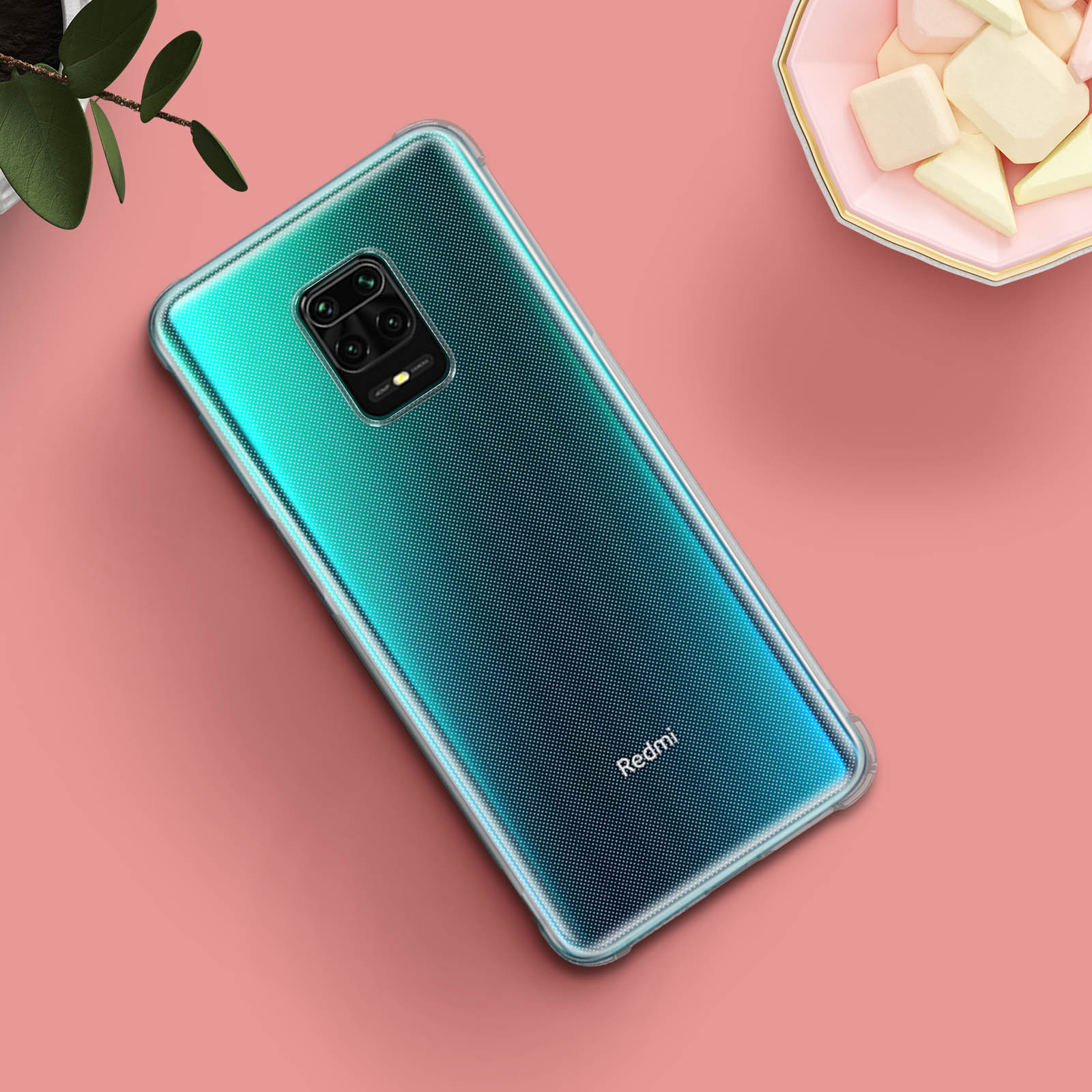 Custodia per telefono con design verde-blu sfumato su superficie rosa. Pianta e marshmallow visibili.