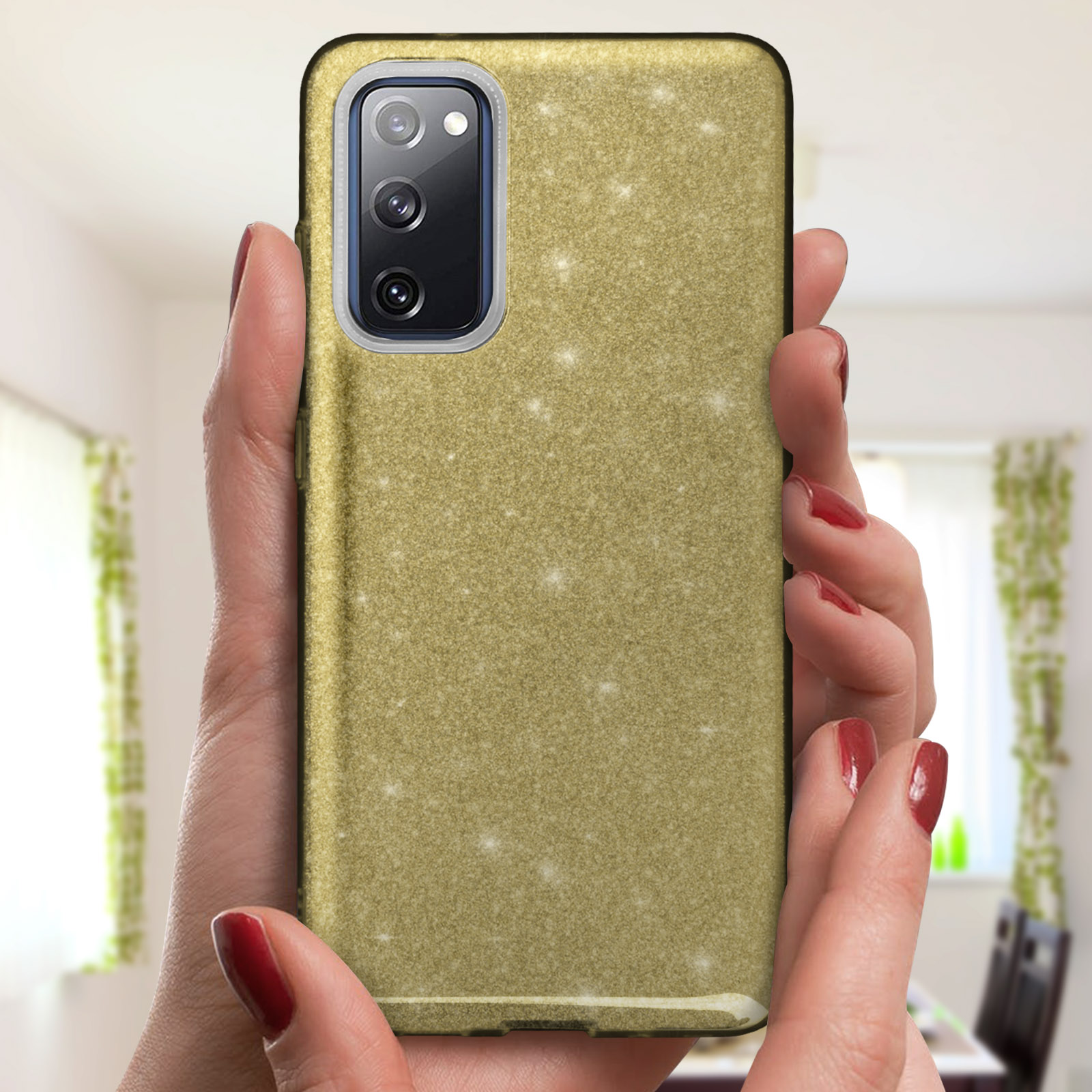 Mani che tengono un telefono con custodia glitterata oro. Unghie rosse, sfondo sfocato.