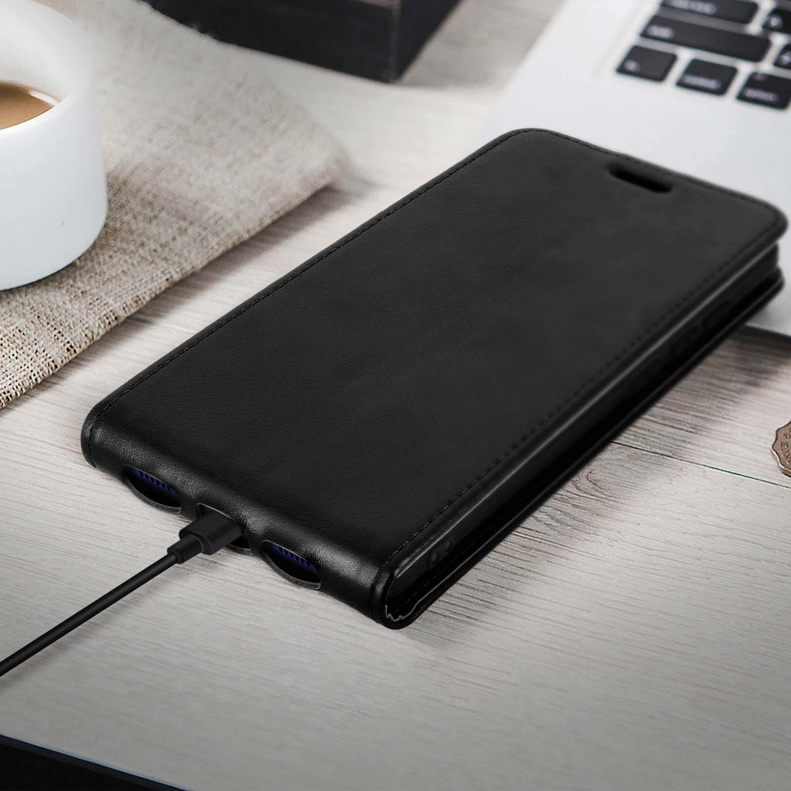 Custodia per telefono in pelle nera con cavo di ricarica collegato. La custodia è appoggiata su una superficie vicino a una tazza.