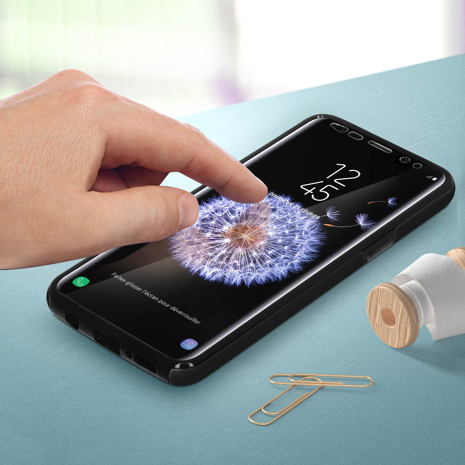 Hand berührt einen Telefonbildschirm mit einem Löwenzahnbild. Das Telefon befindet sich in einer Hülle und auf einem blauen Tisch.