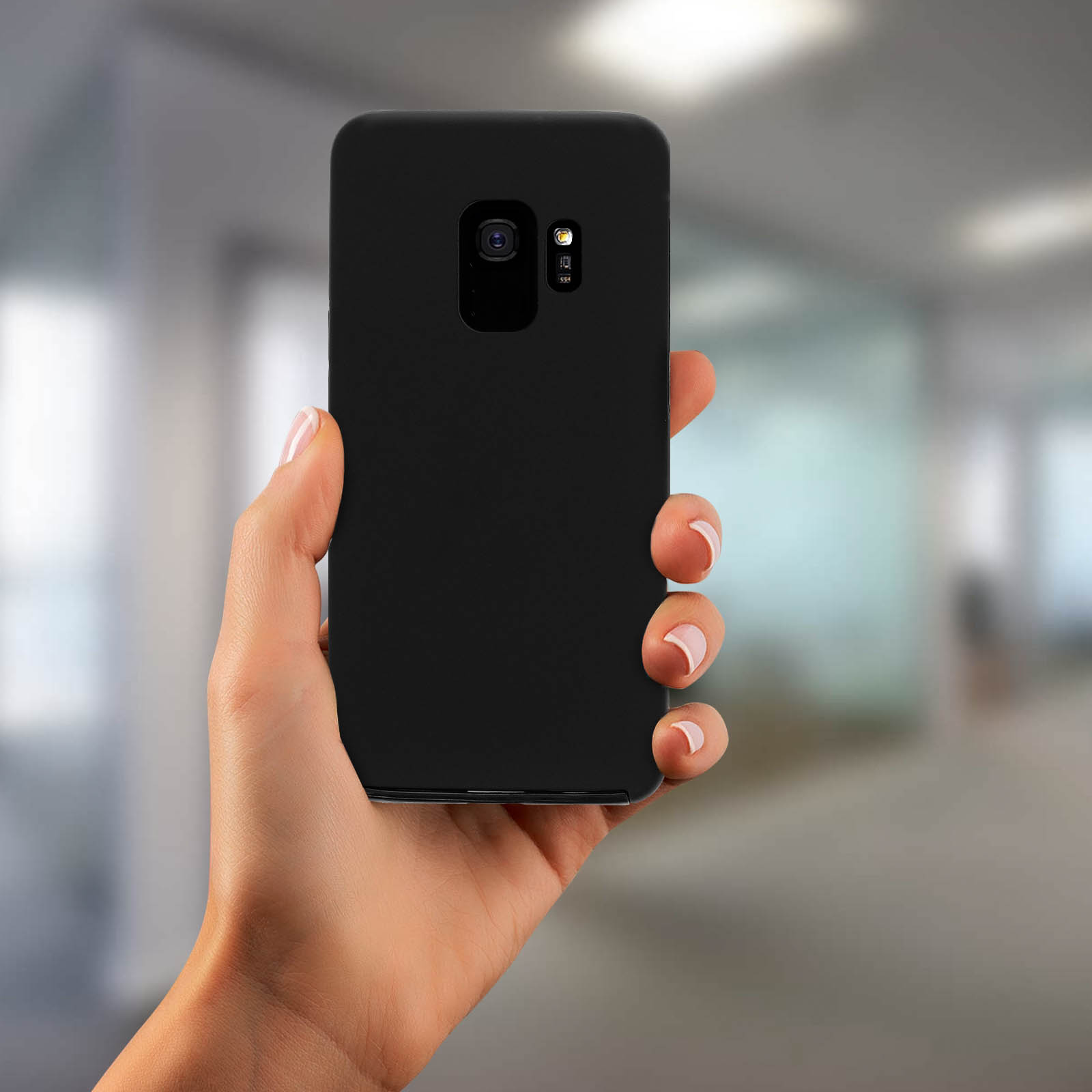 Eine Hand hält ein schwarzes Telefon mit verschwommenem Bürohintergrund.