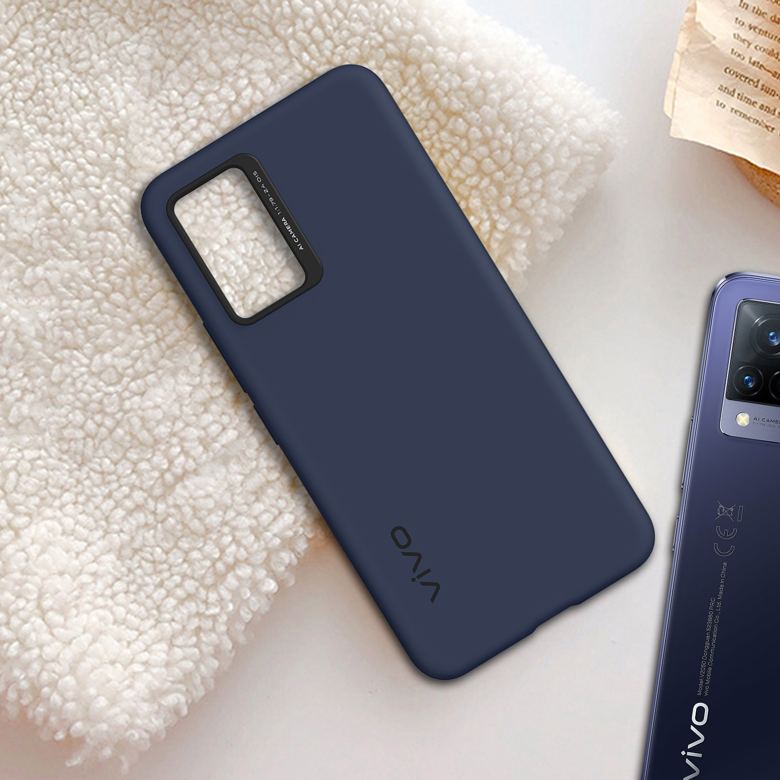 Una custodia per telefono blu scuro su una coperta bianca e soffice, con un telefono accanto. C'è 'vivo' sopra.