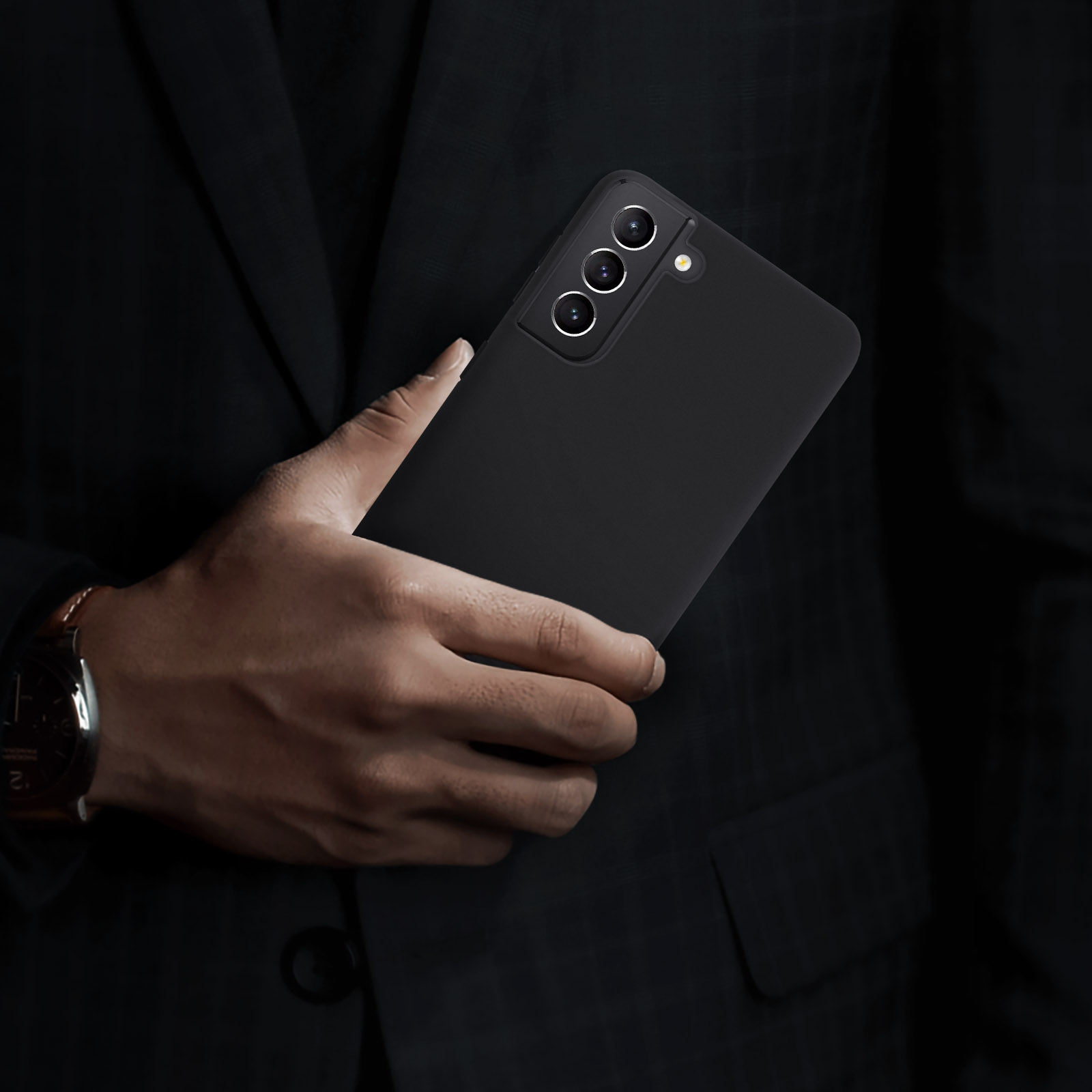 Un uomo che tiene un telefono nero in una custodia. Indossa un abito.