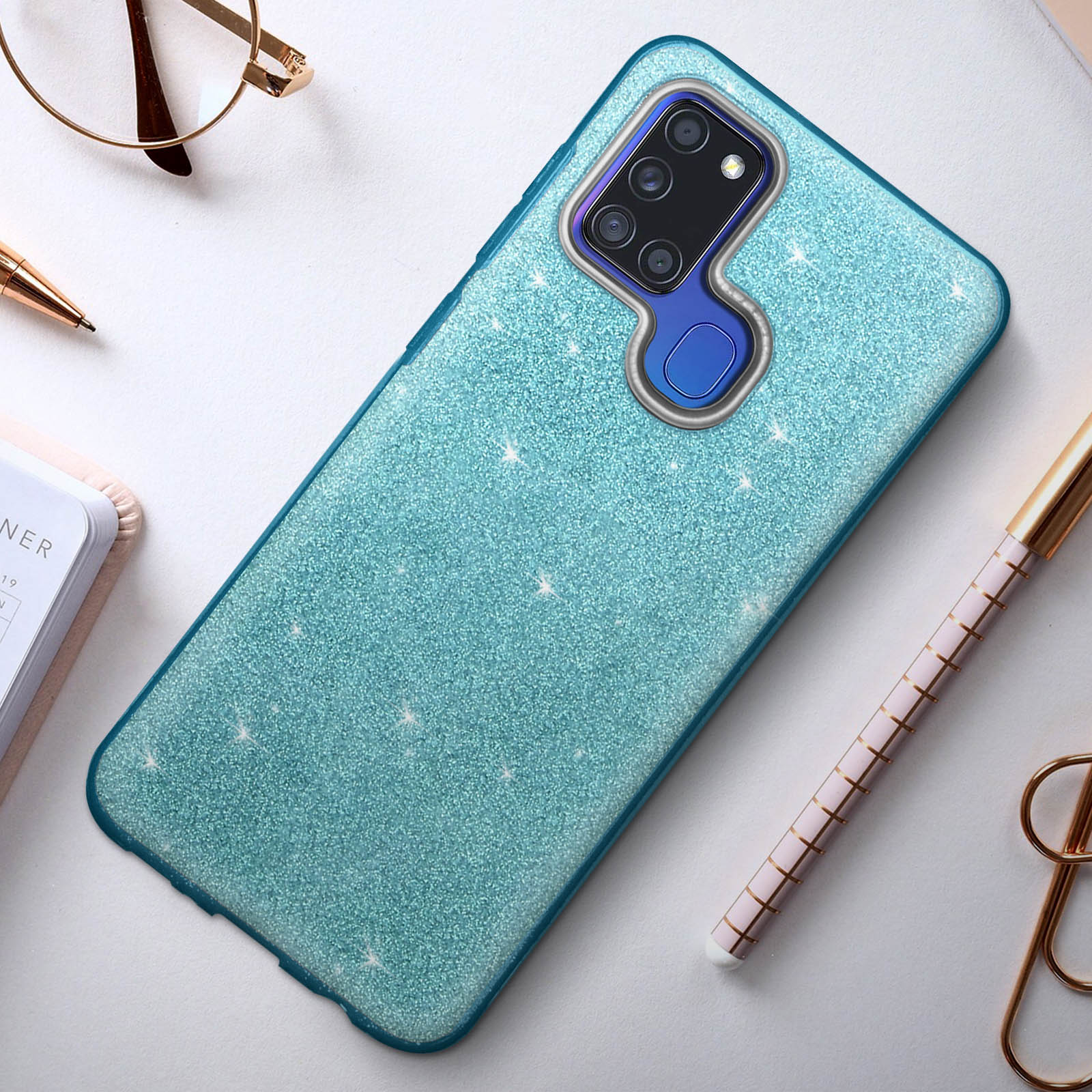 Coque de téléphone bleu pailleté avec téléphone sur table, stylo et lunettes.