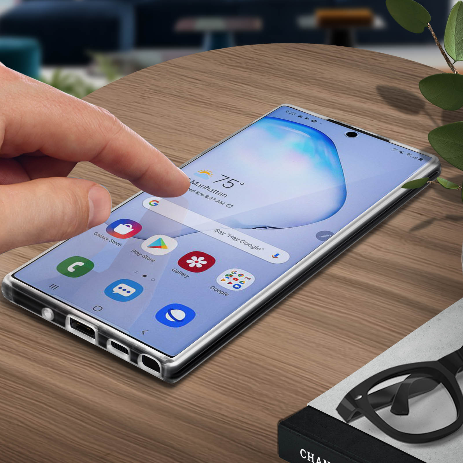 Une main touche l'écran d'un téléphone affichant une appli météo, sur une table en bois.