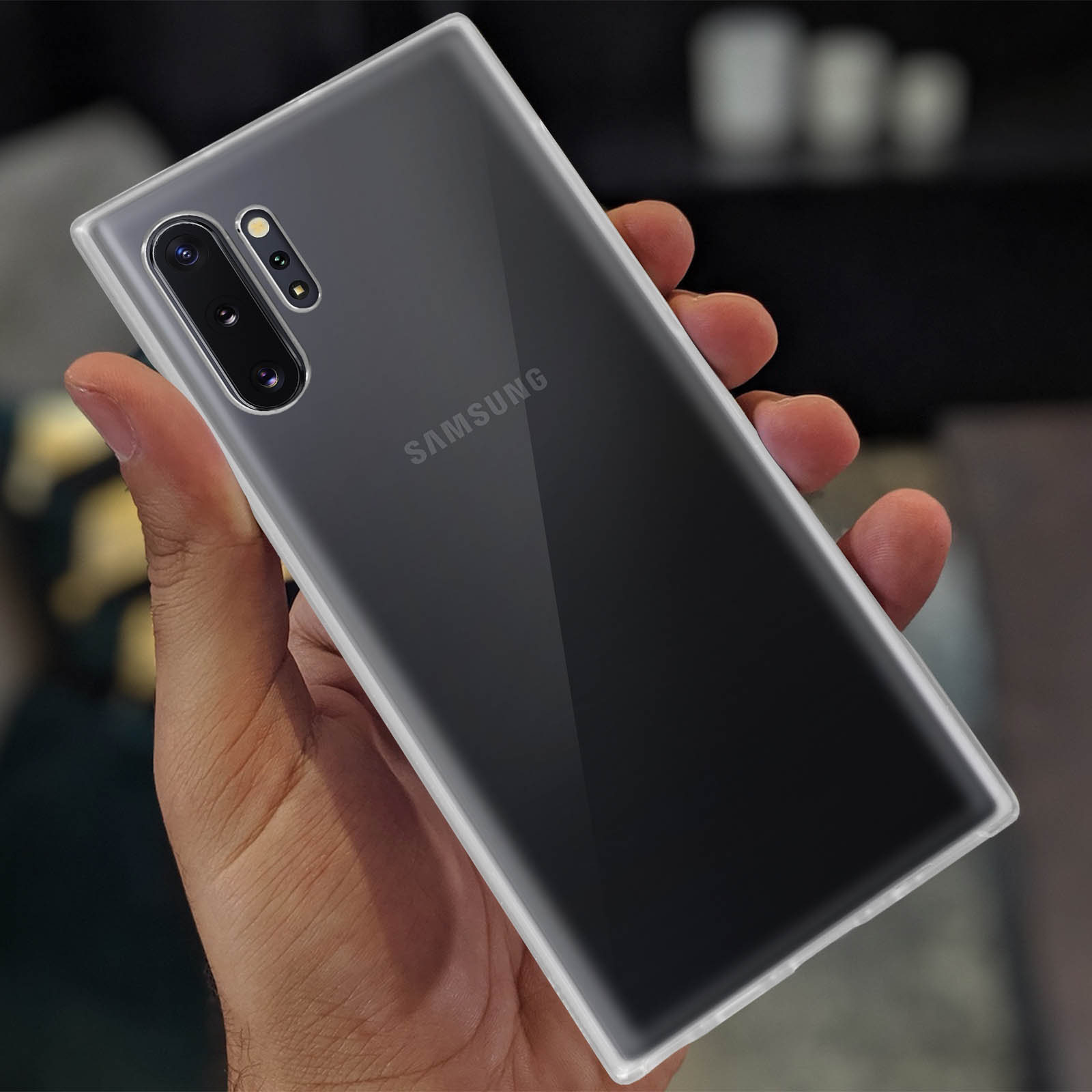 Main tenant un téléphone dans un étui transparent. Le téléphone est un Samsung. Le fond est sombre avec un effet flou.