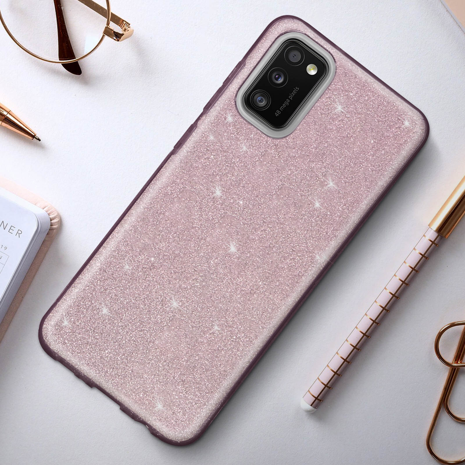 Een roze glittertelefoonhoesje op een bureau met een pen en bril.