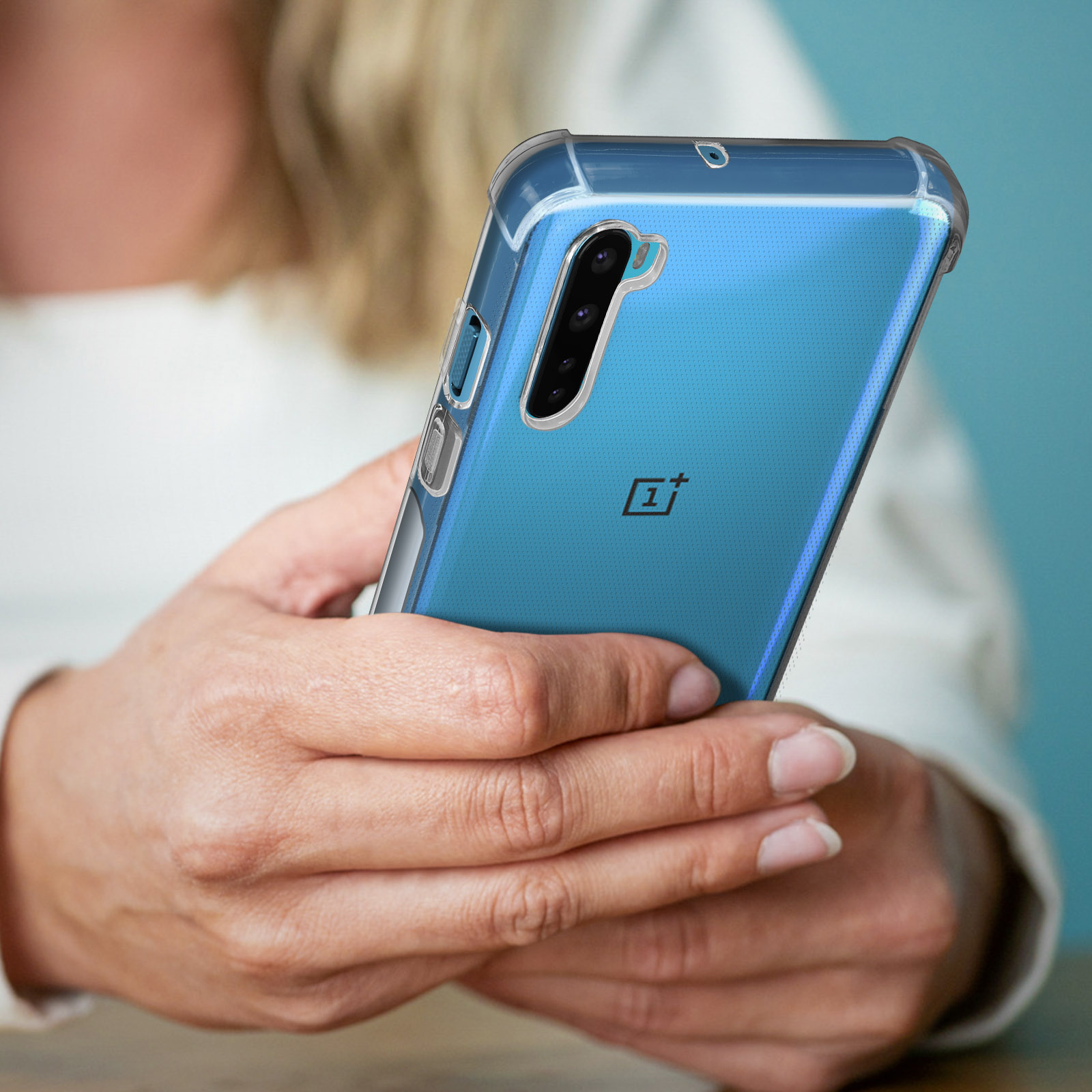 Una persona tiene in mano un telefono in una custodia trasparente, contro un muro blu.