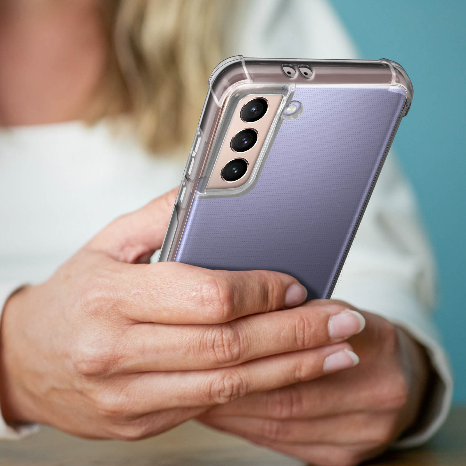 Primo piano di una donna che tiene un telefono in una custodia trasparente. Lo sfondo è un muro blu sfocato.