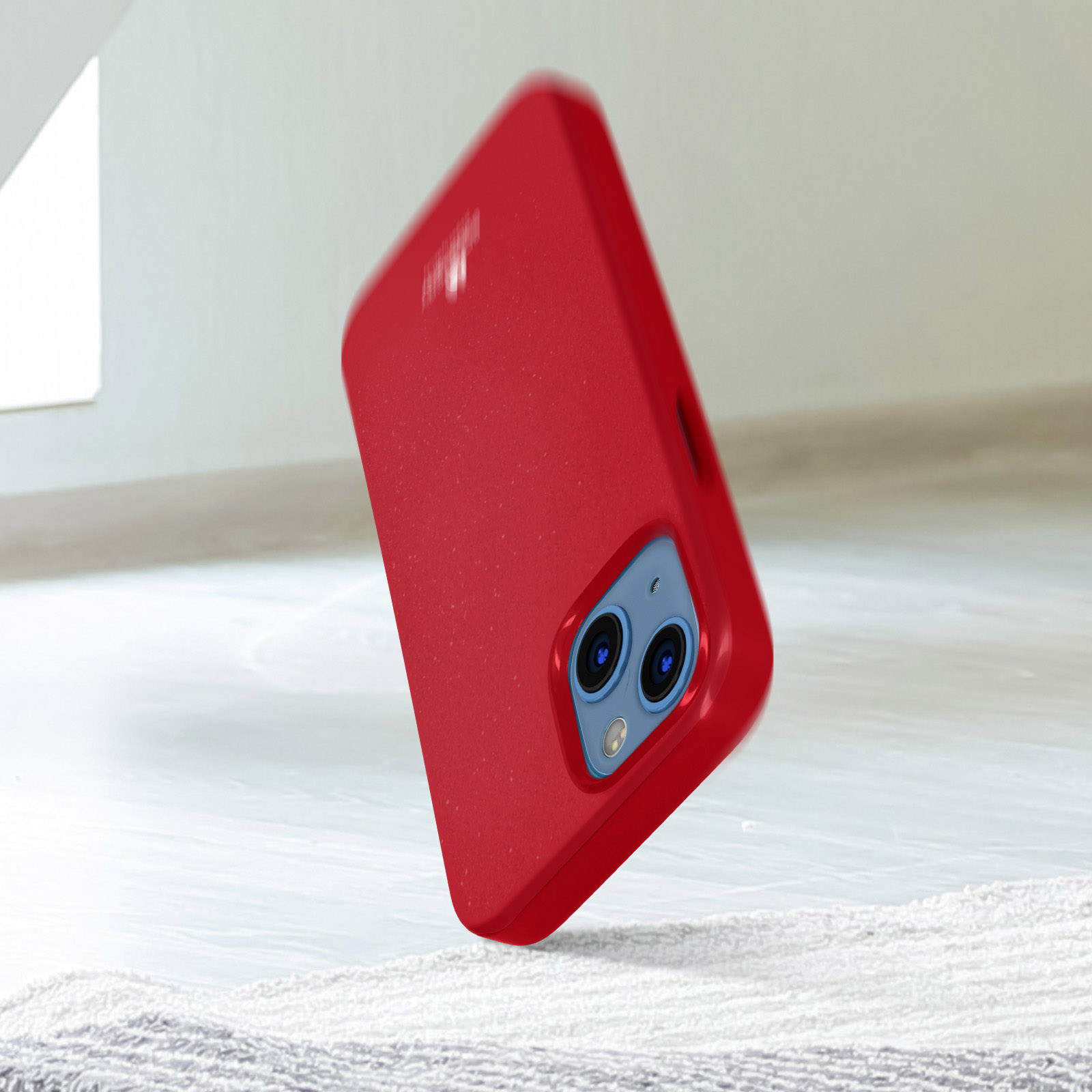 Una custodia rossa per telefono sta cadendo. La custodia ha due fotocamere. È su una superficie chiara.