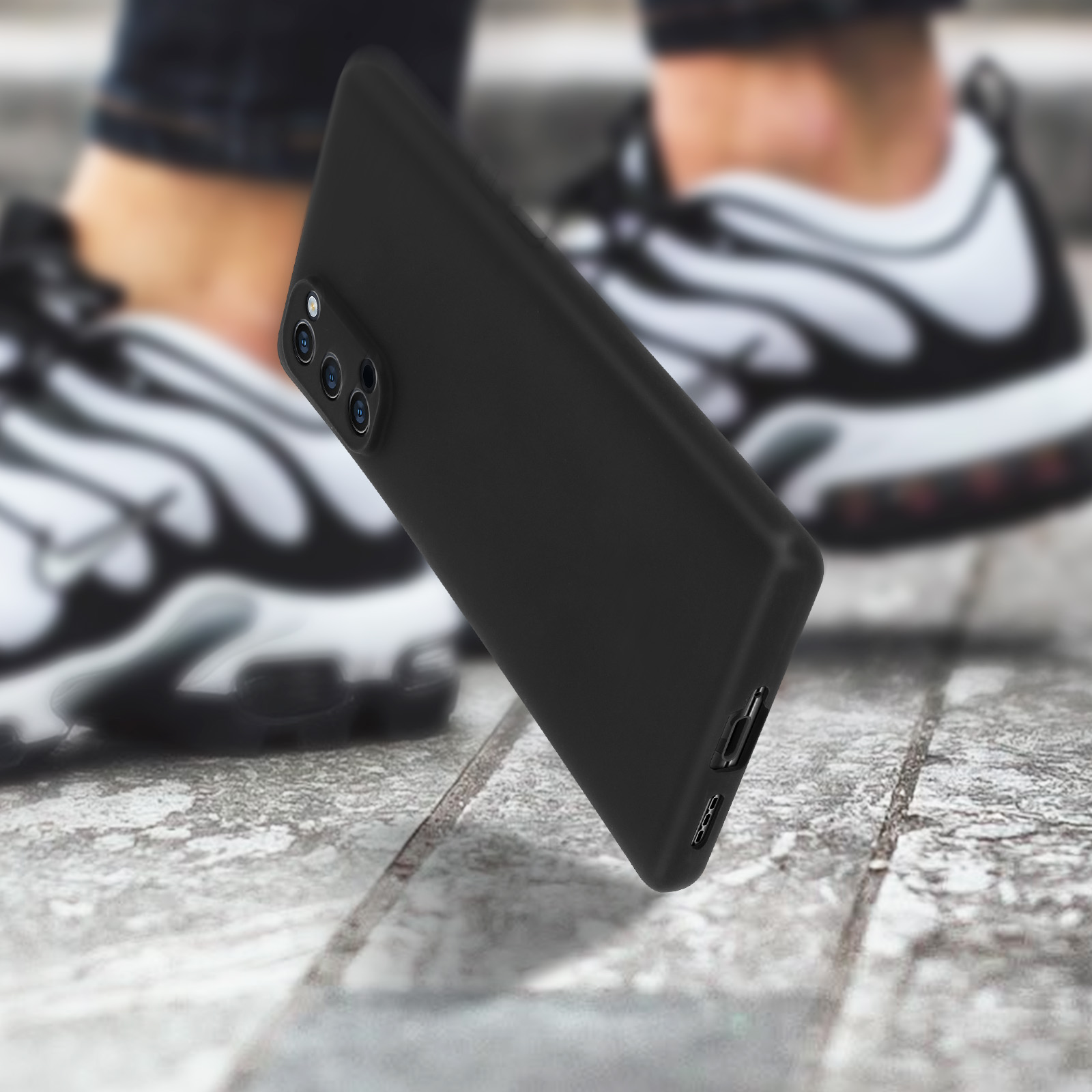 Custodia nera per telefono su superficie in cemento con scarpe da ginnastica sfocate sullo sfondo, focus sulla custodia.
