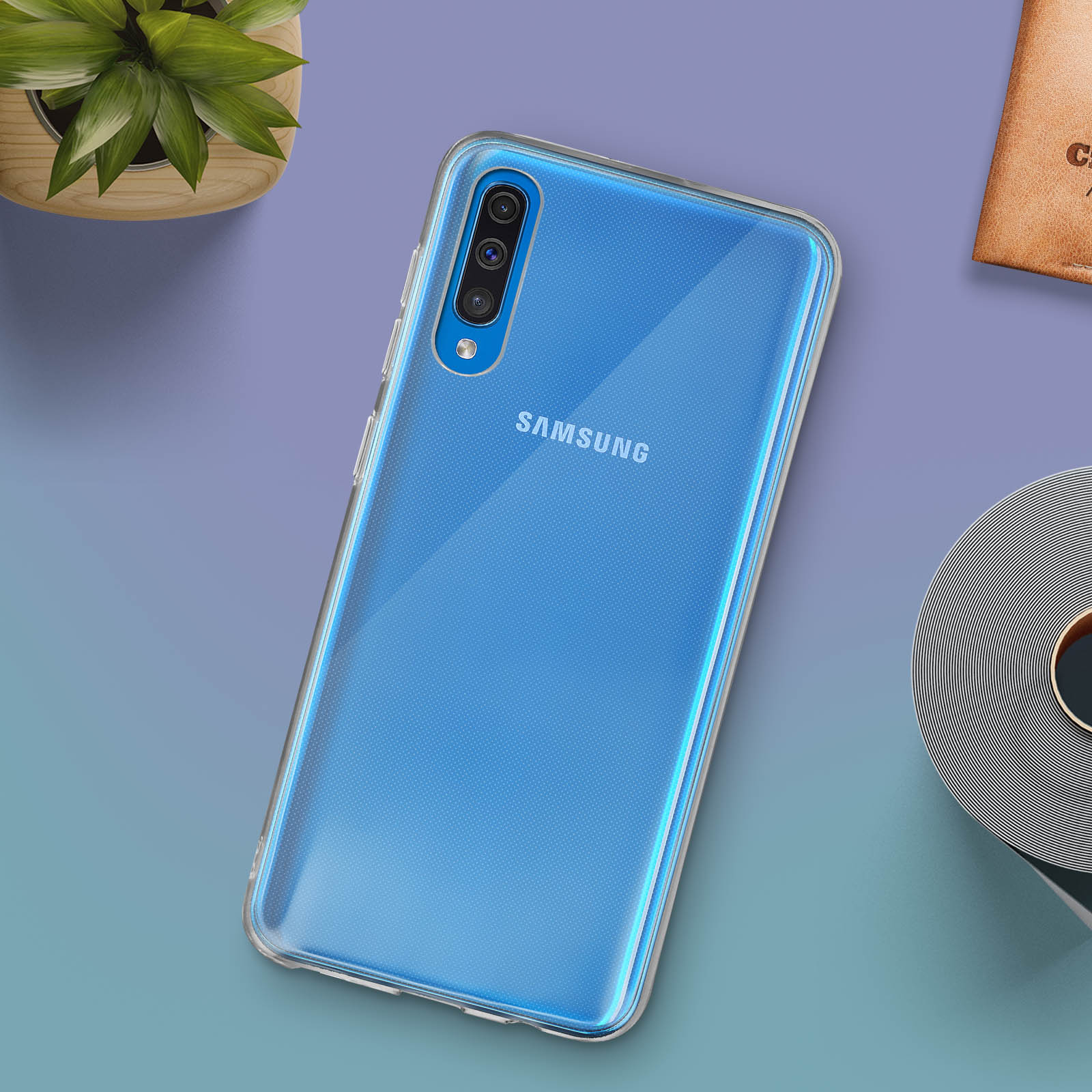 Una custodia trasparente per telefono su un telefono blu con SAMSUNG visibile. Una pianta e un libro sono vicini.