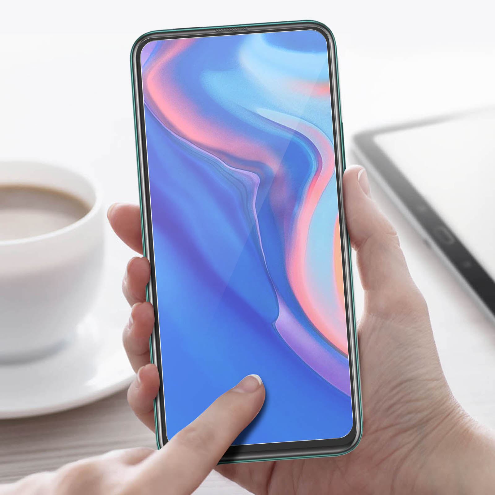 Een hand die een smartphone met een blauw scherm vasthoudt. Een vinger raakt het scherm aan. Een kopje en een tablet op de achtergrond.