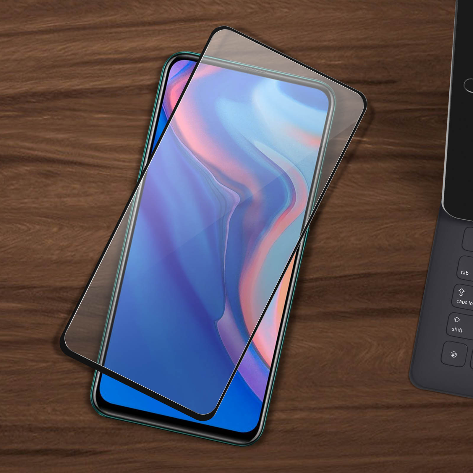 Een telefoon met een schermbeschermer op een houten oppervlak. Een toetsenbord staat rechts.