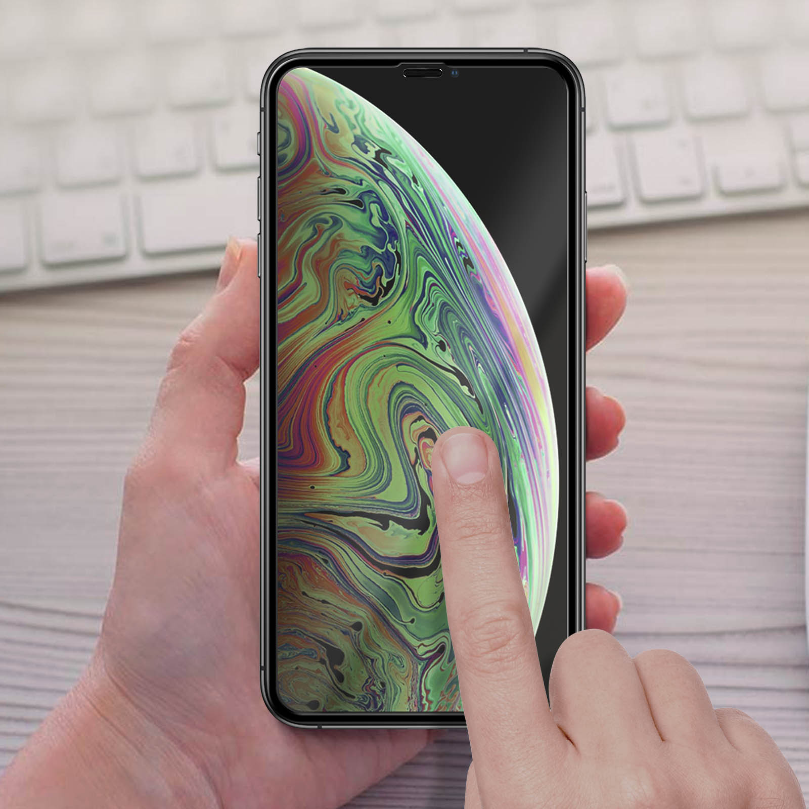 Mano che tiene un telefono che mostra un motivo colorato e vorticoso. Dito tocca lo schermo. Tastiera sullo sfondo.