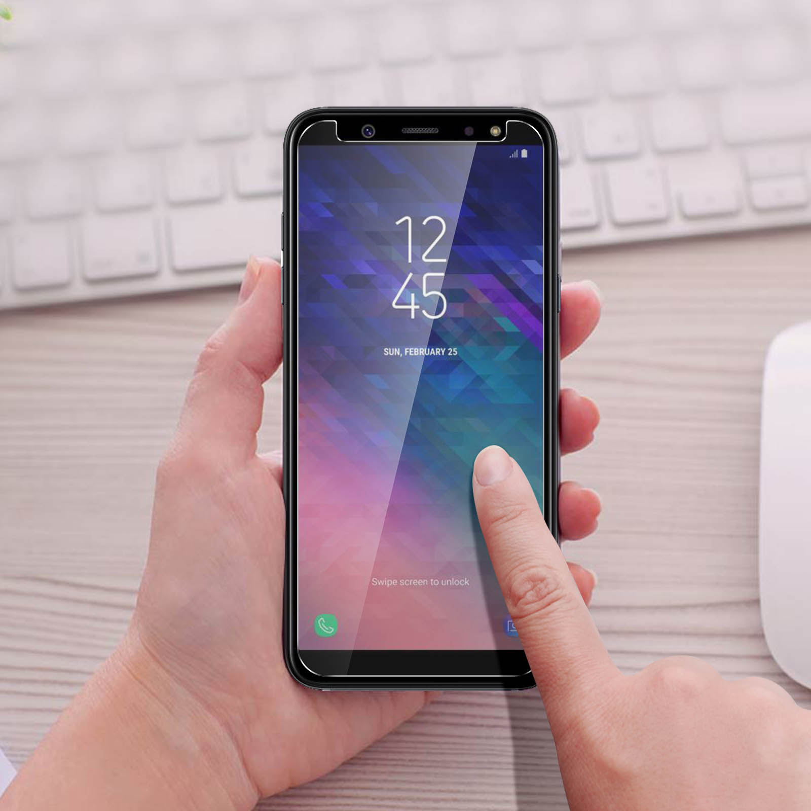 Una mano tocca lo schermo di un telefono che mostra l'ora. Tastiera e mouse sullo sfondo.