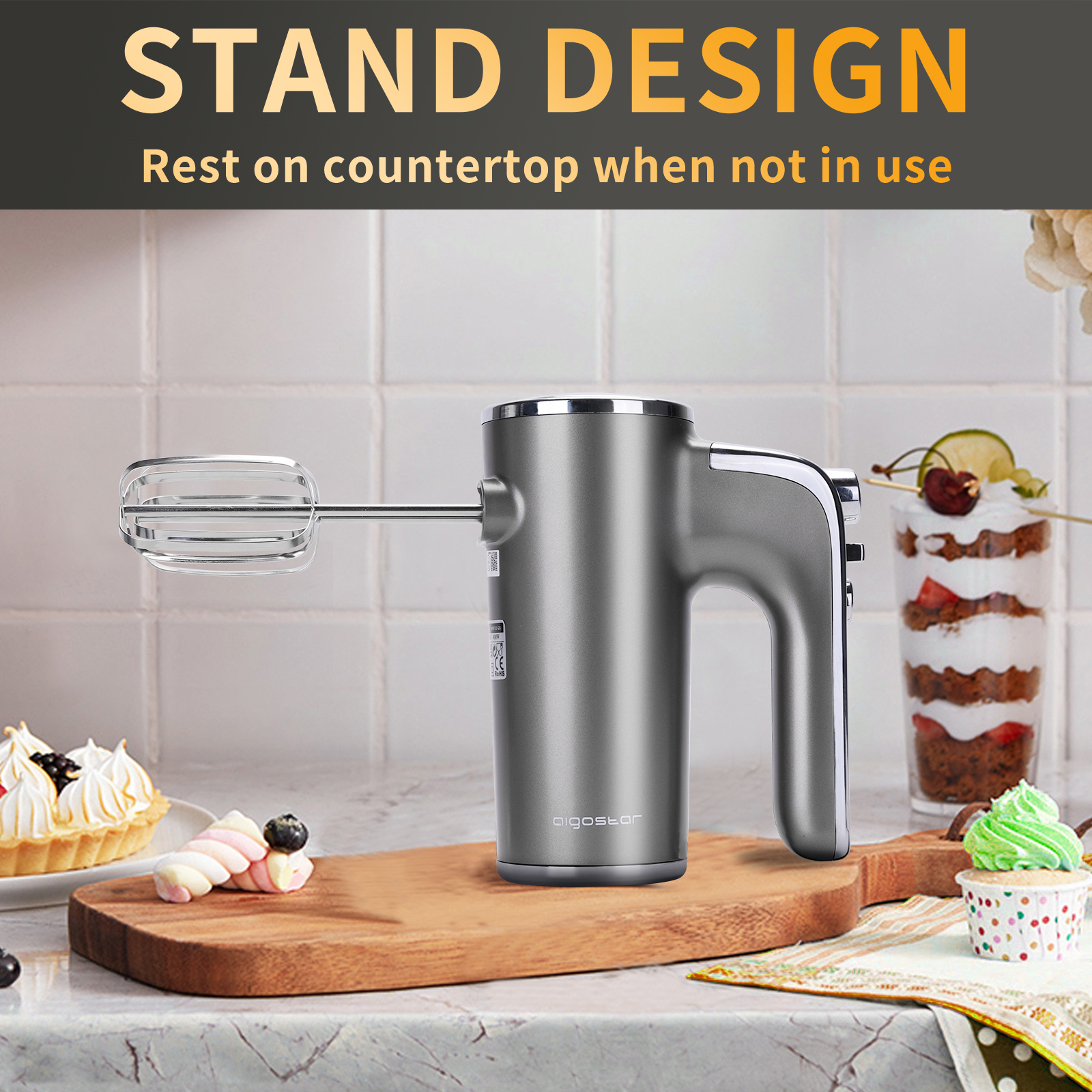 Silberner Handmixer auf einem Holzbrett mit Backwaren. Text lautet STAND DESIGN.