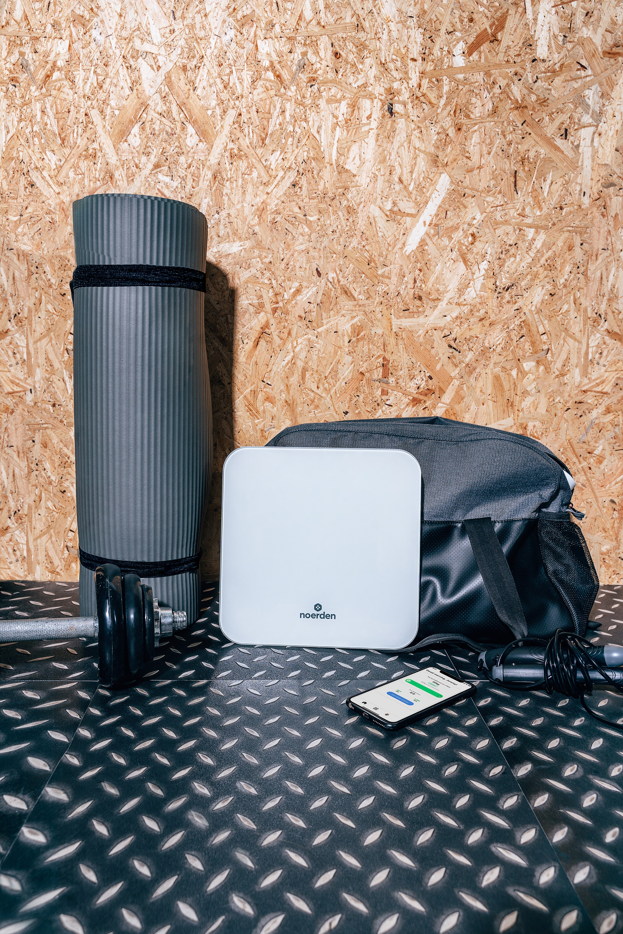Fitnessgeräte: Matte, Waage, Tasche, Hantel, Telefon und Springseil auf strukturierter Oberfläche.