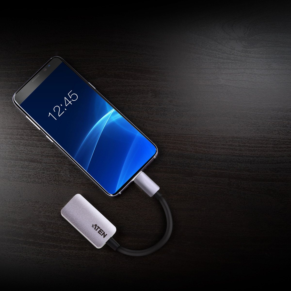 Ein silberner Adapter, verbunden mit einem Smartphone und einem schwarzen Kabel auf dunkler Holzoberfläche.