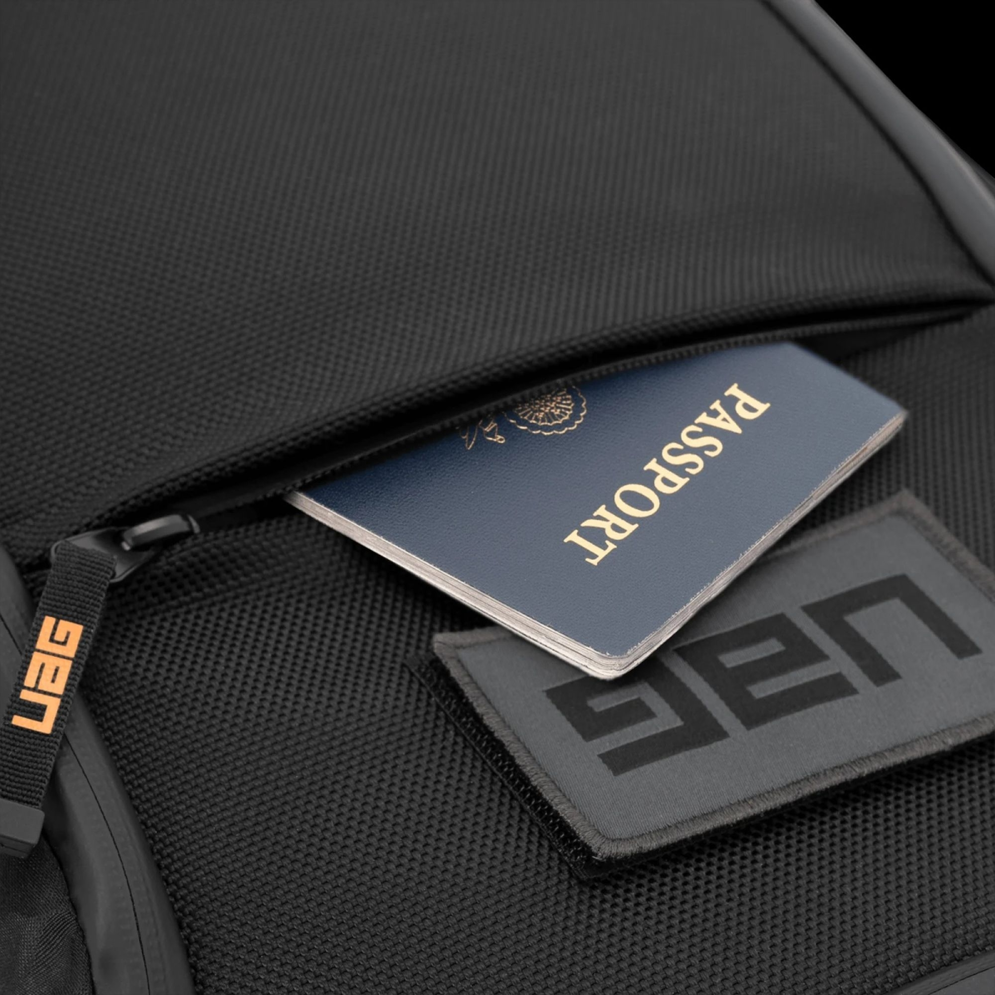 Ein Reisepass teilweise sichtbar in einer schwarzen UAG-Rucksacktasche mit UAG-Logo.
