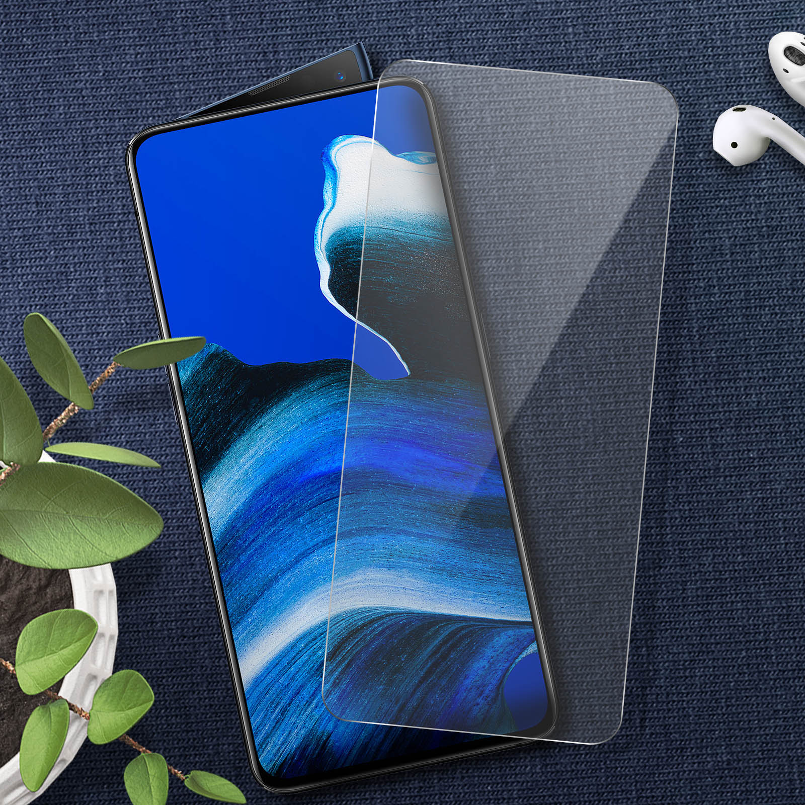 Un telefono blu con protezione schermo e auricolari wireless su tessuto blu. Una pianta a sinistra.