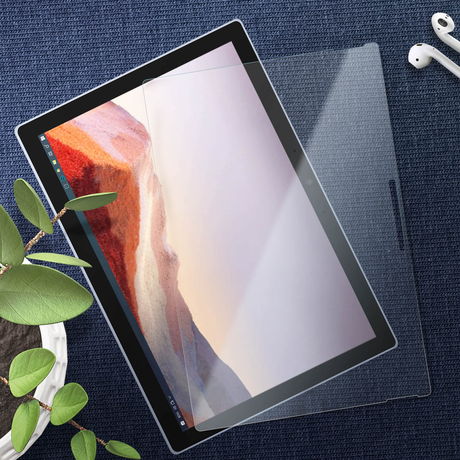 Tablet con protezione schermo, con una pianta e auricolari sullo sfondo. Lo schermo mostra l'interfaccia di Windows.