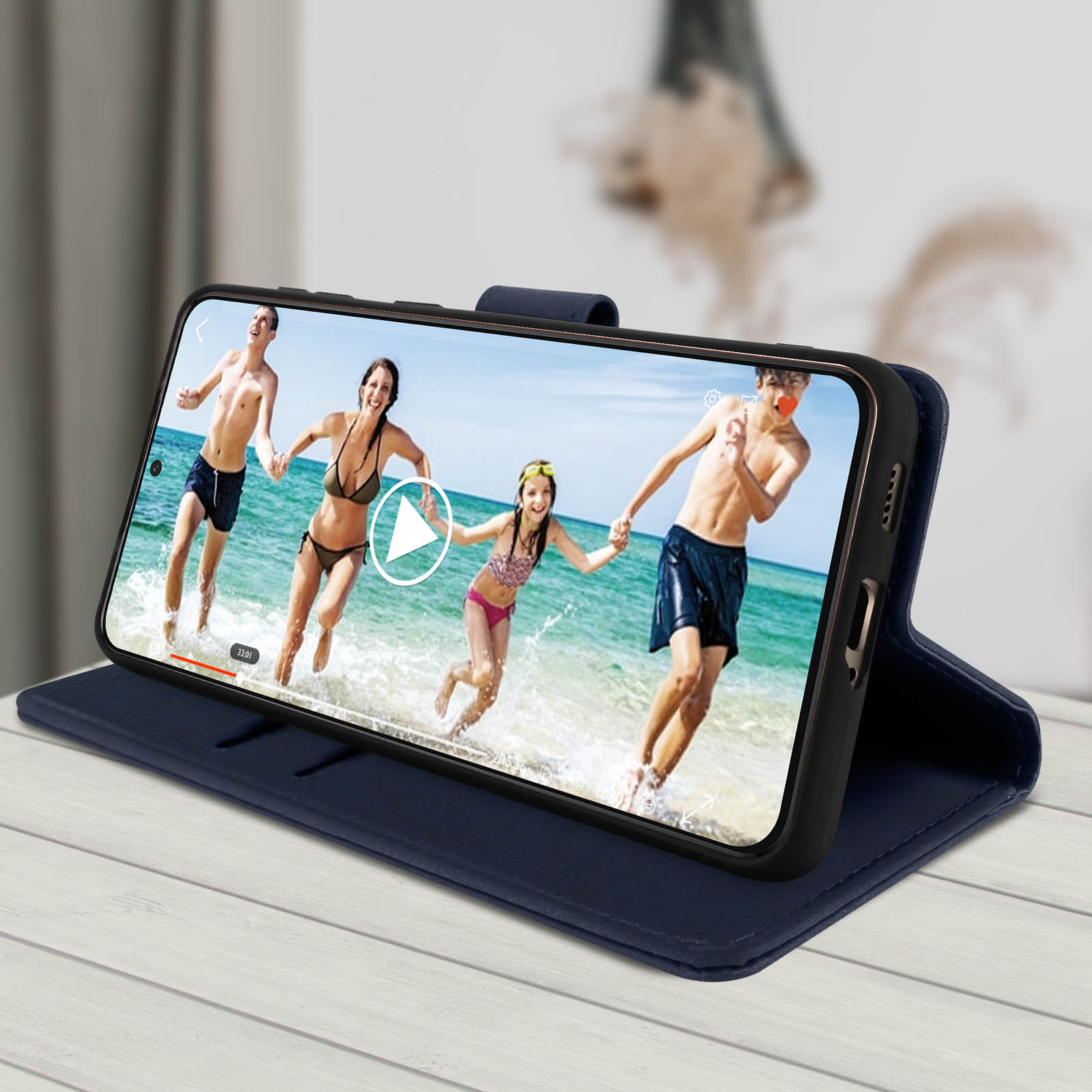 Telefono in una custodia blu mostra un video di persone in spiaggia. La custodia è aperta su un tavolo.