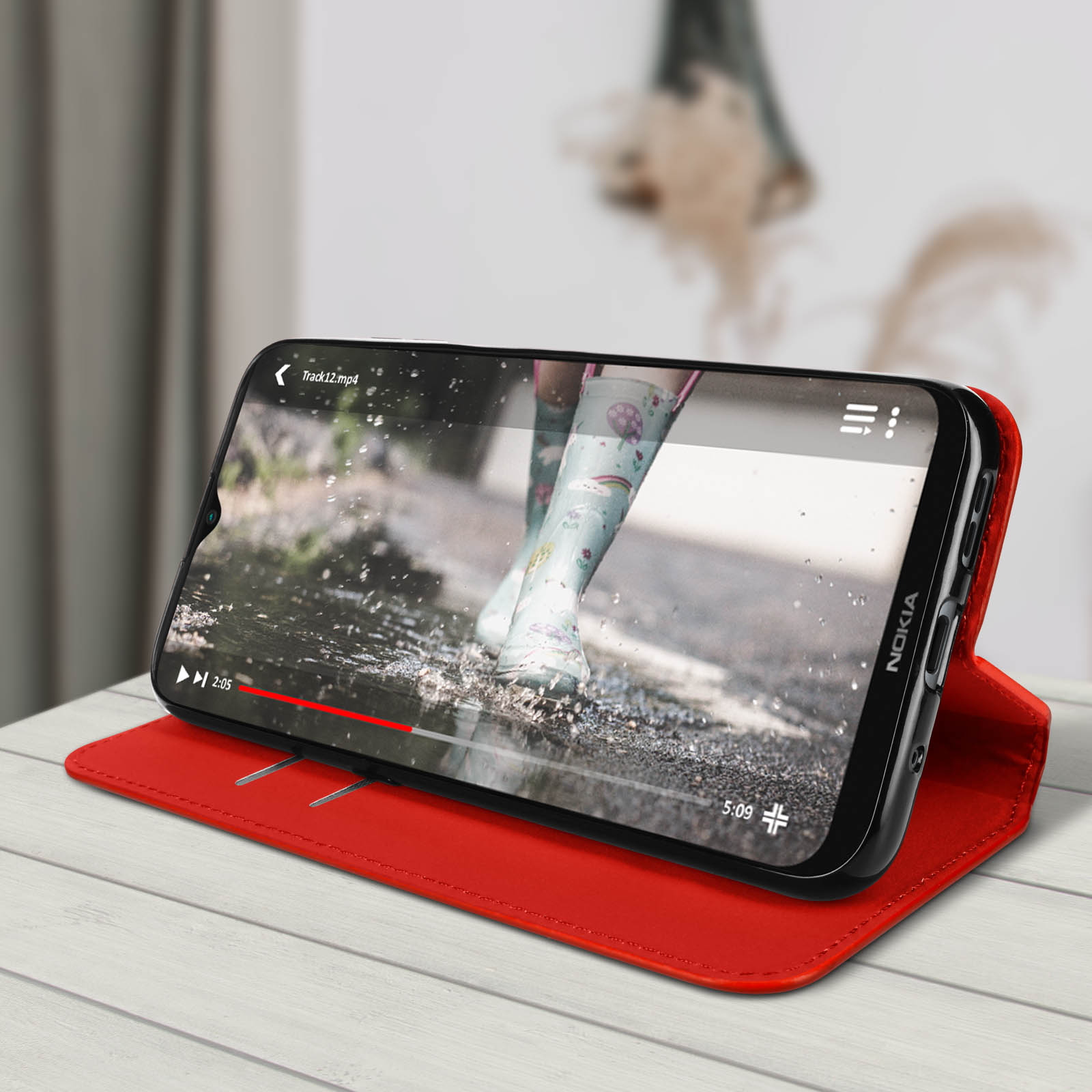 Un telefono mostra un video su un tavolo di legno, appoggiato su una custodia rossa, sfondo sfocato.