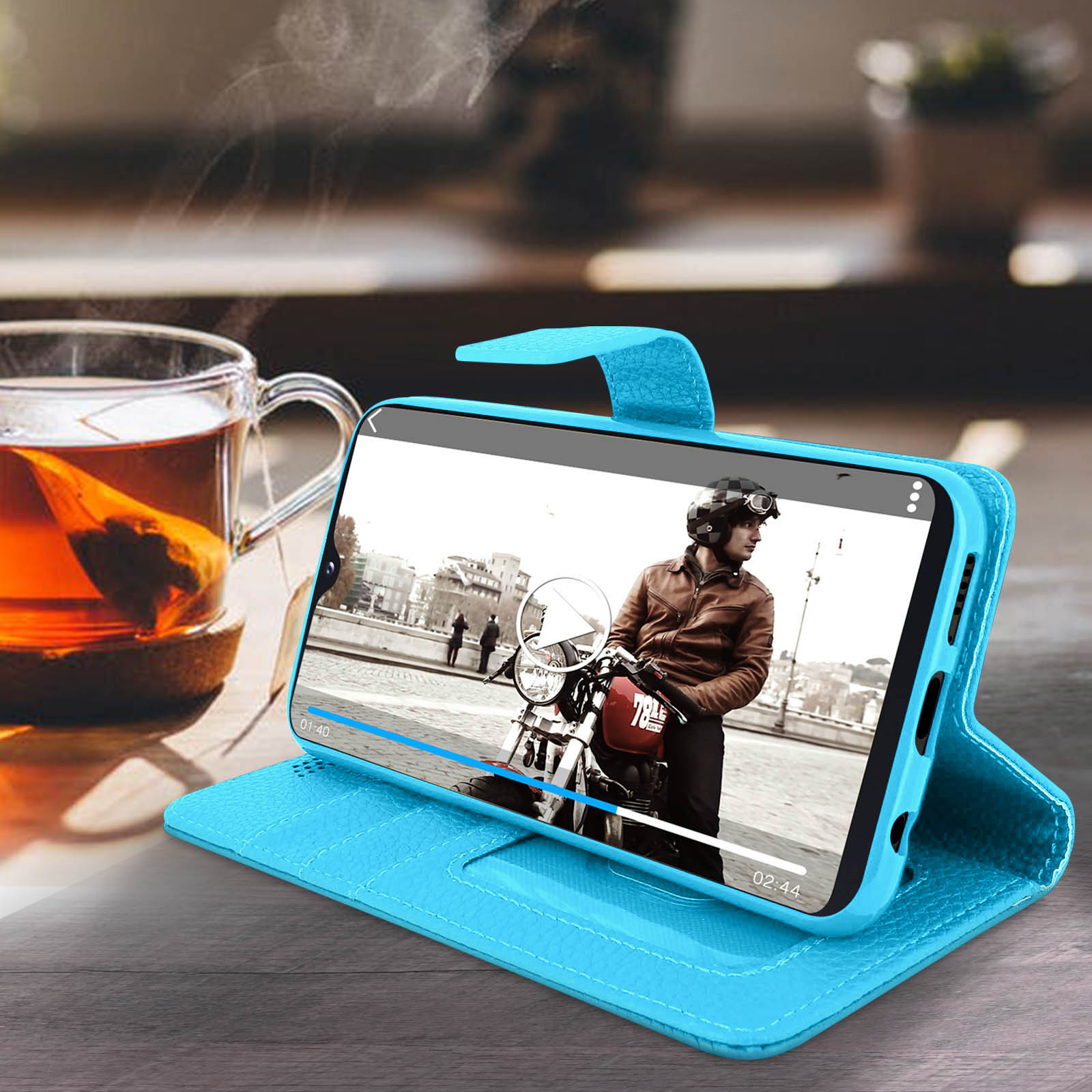 Un téléphone dans un étui bleu jouant une vidéo d'un motard. Une tasse de thé est à gauche.