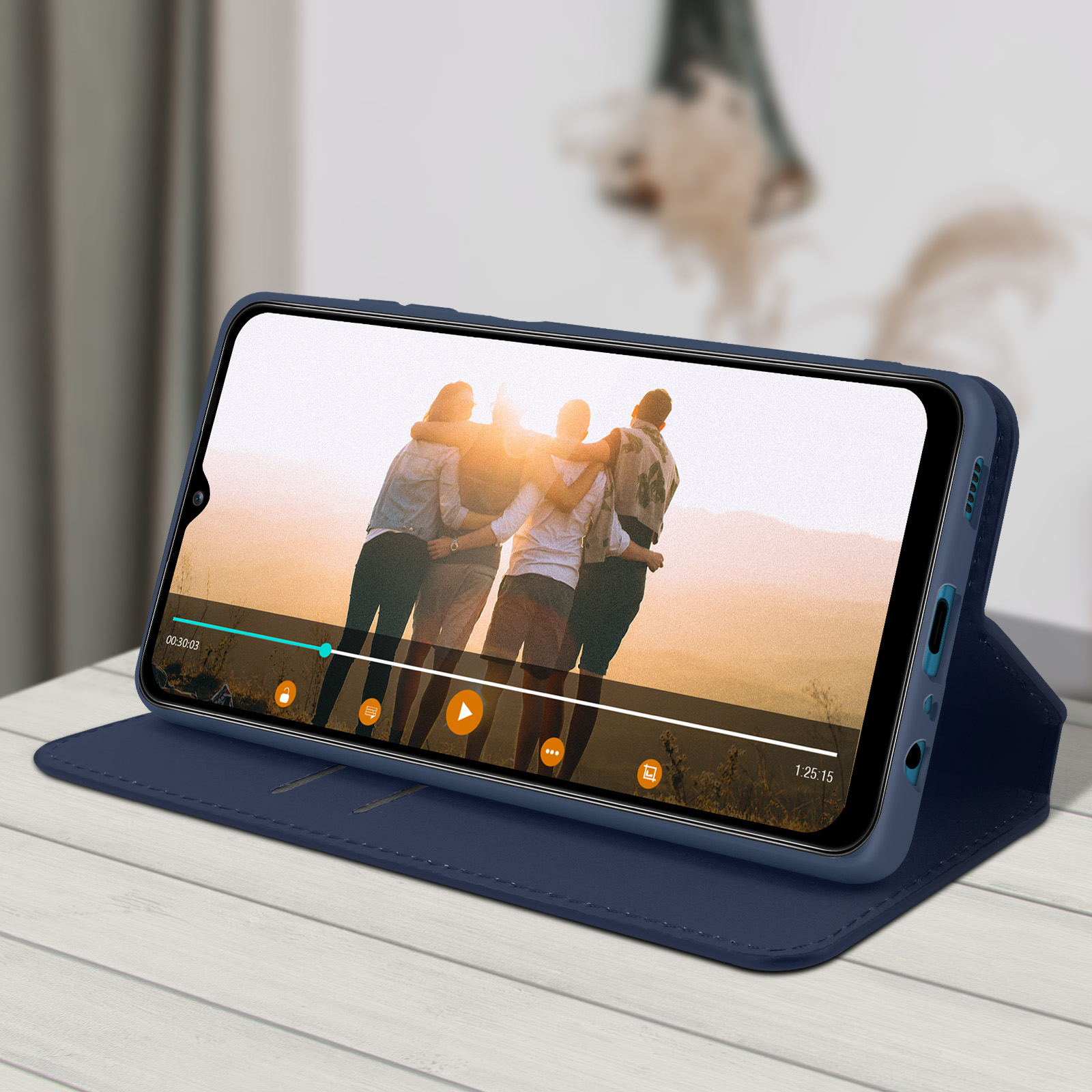 Téléphone dans un étui bleu affichant une vidéo d'un groupe s'embrassant. Table blanche et arrière-plan flou.