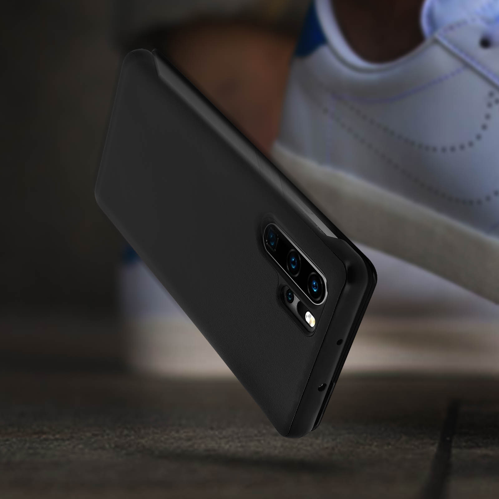 Una custodia per telefono nera, il telefono è su una superficie di legno, con una scarpa sfocata sullo sfondo.