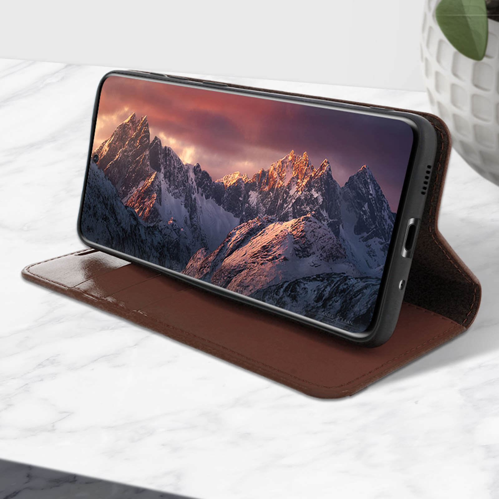 Een telefoon met een bruine hoes toont een afbeelding op een marmeren oppervlak. De hoes is open.
