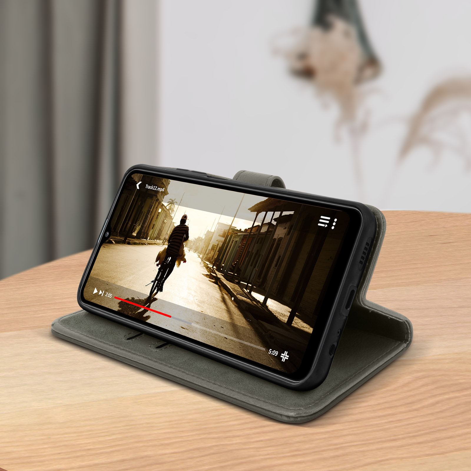 Ein Telefon in einer grauen Hülle zeigt ein Video eines Radfahrers. Das Telefon liegt auf einem Holztisch. Unscharfer Hintergrund.