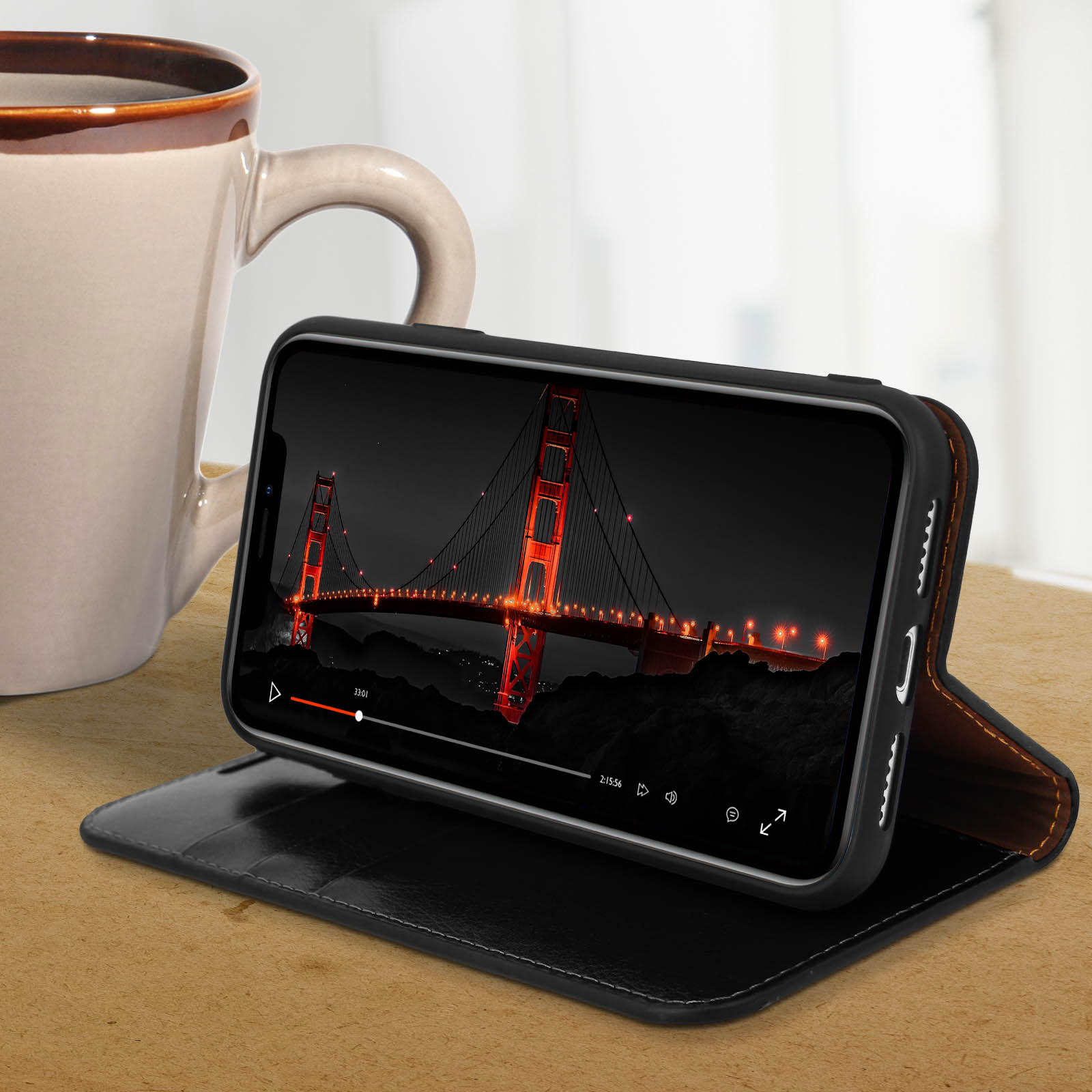 Un telefono in una custodia nera, che mostra il Golden Gate Bridge. Una tazza è a sinistra del telefono.