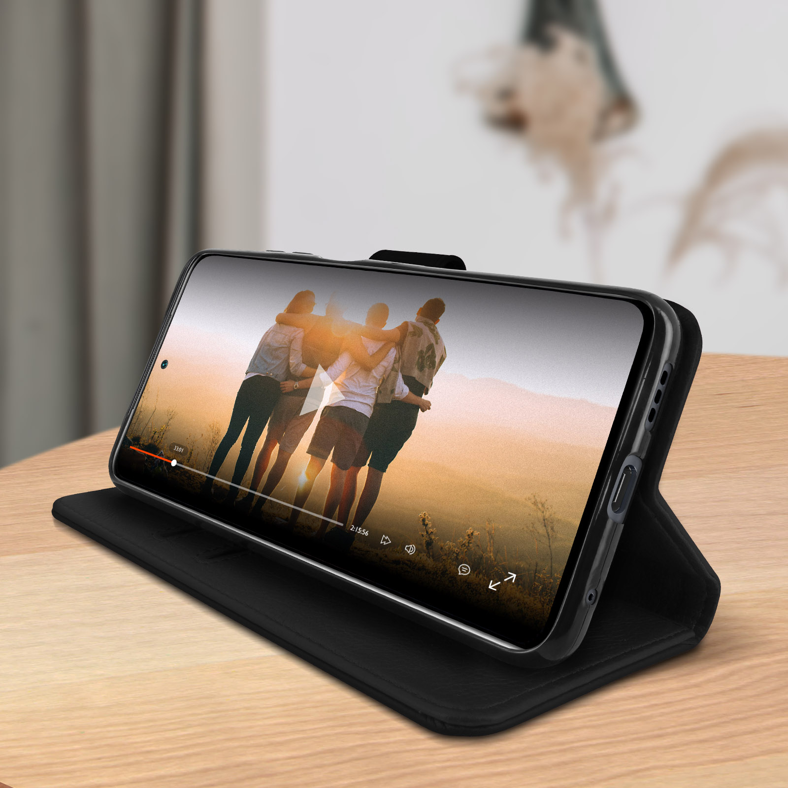 Zwarte telefoonhoes met een telefoon die een video toont. De hoes ligt op een houten tafel.