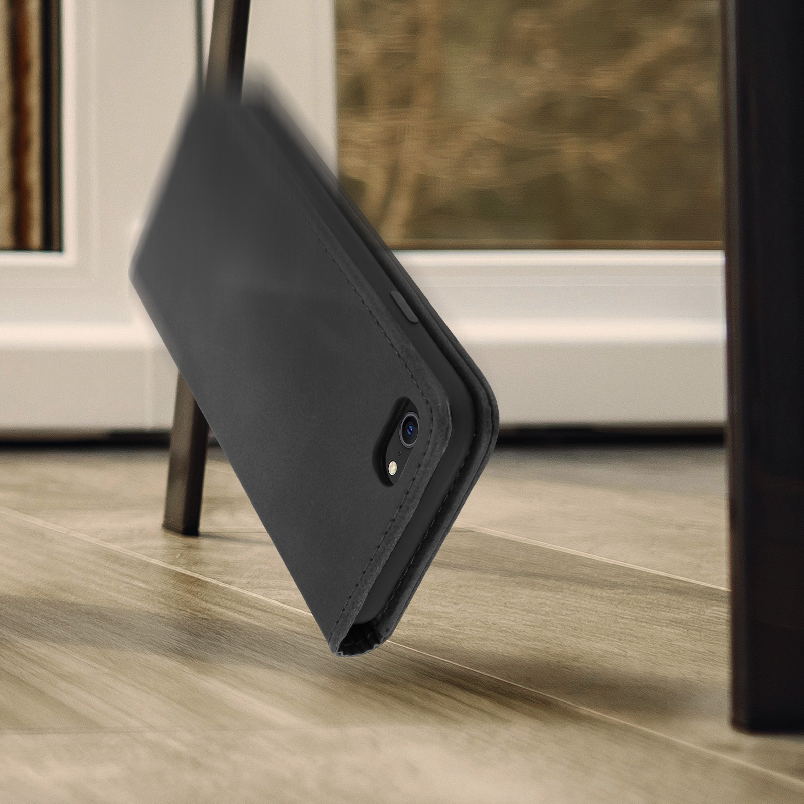 Una custodia per telefono nera sta cadendo su un pavimento di legno. La custodia è aperta.