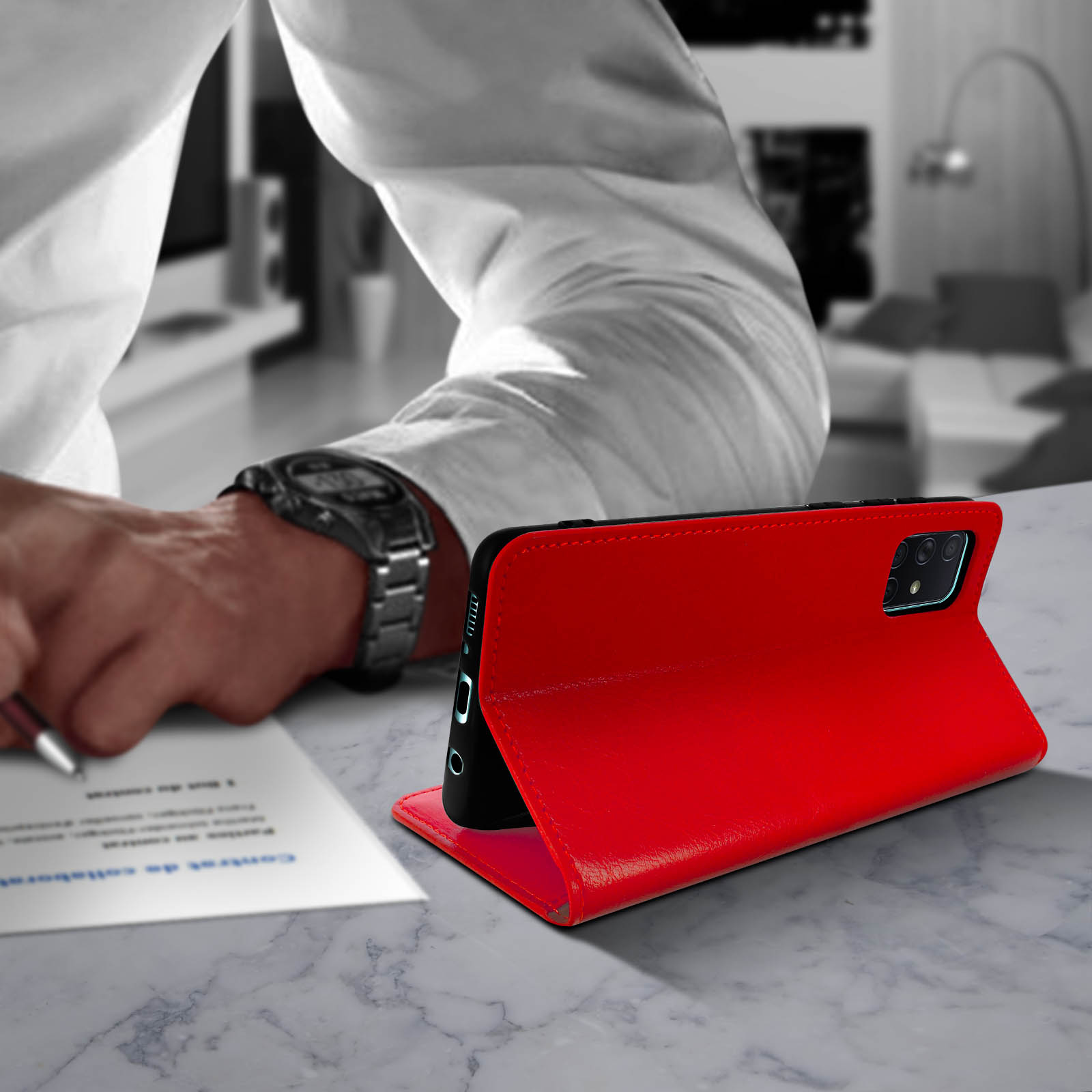 Una persona che scrive, con una custodia rossa per telefono in primo piano, su una superficie di marmo.