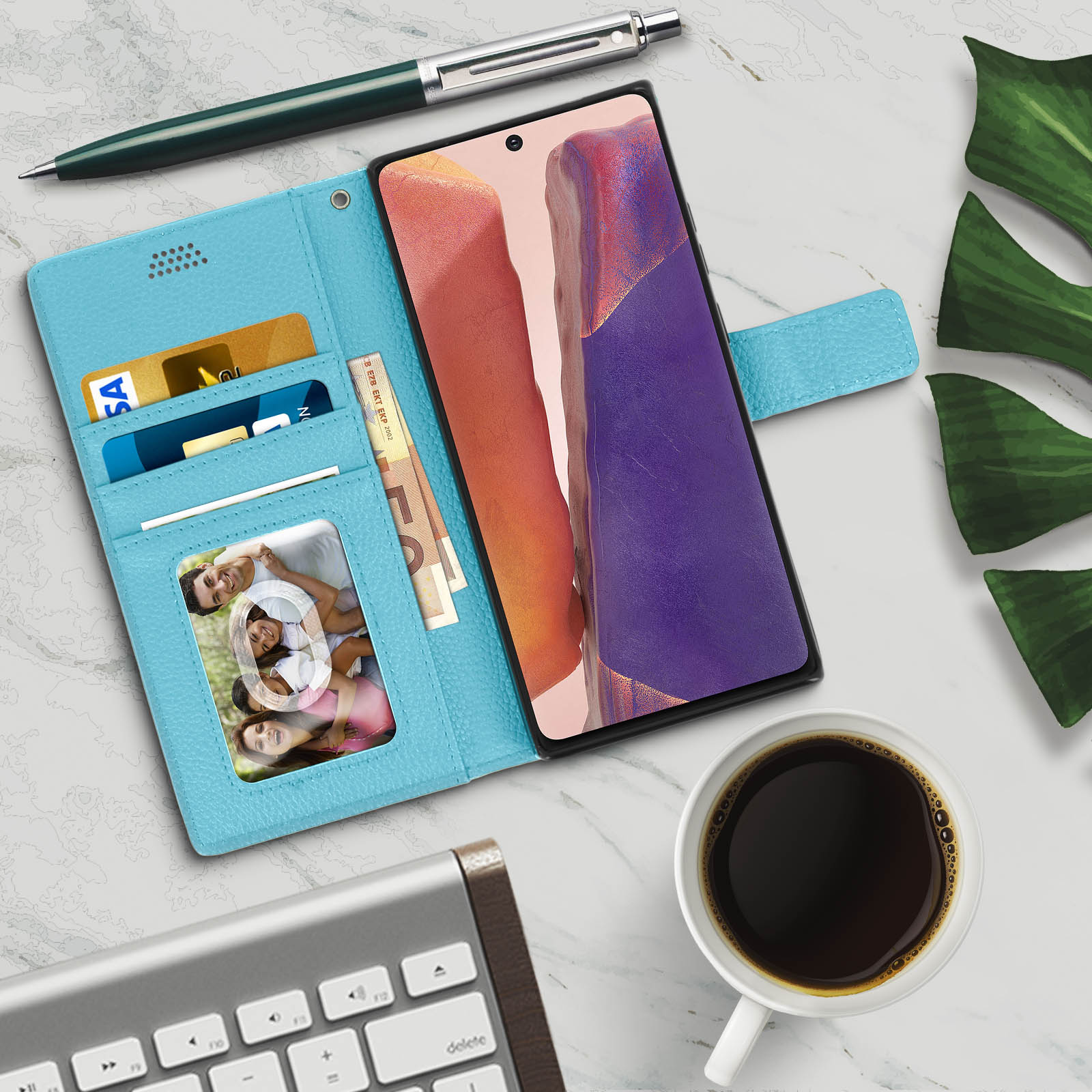 Custodia blu per telefono aperta, con carte, contanti, foto. Telefono a destra, con tazza di caffè e tastiera.