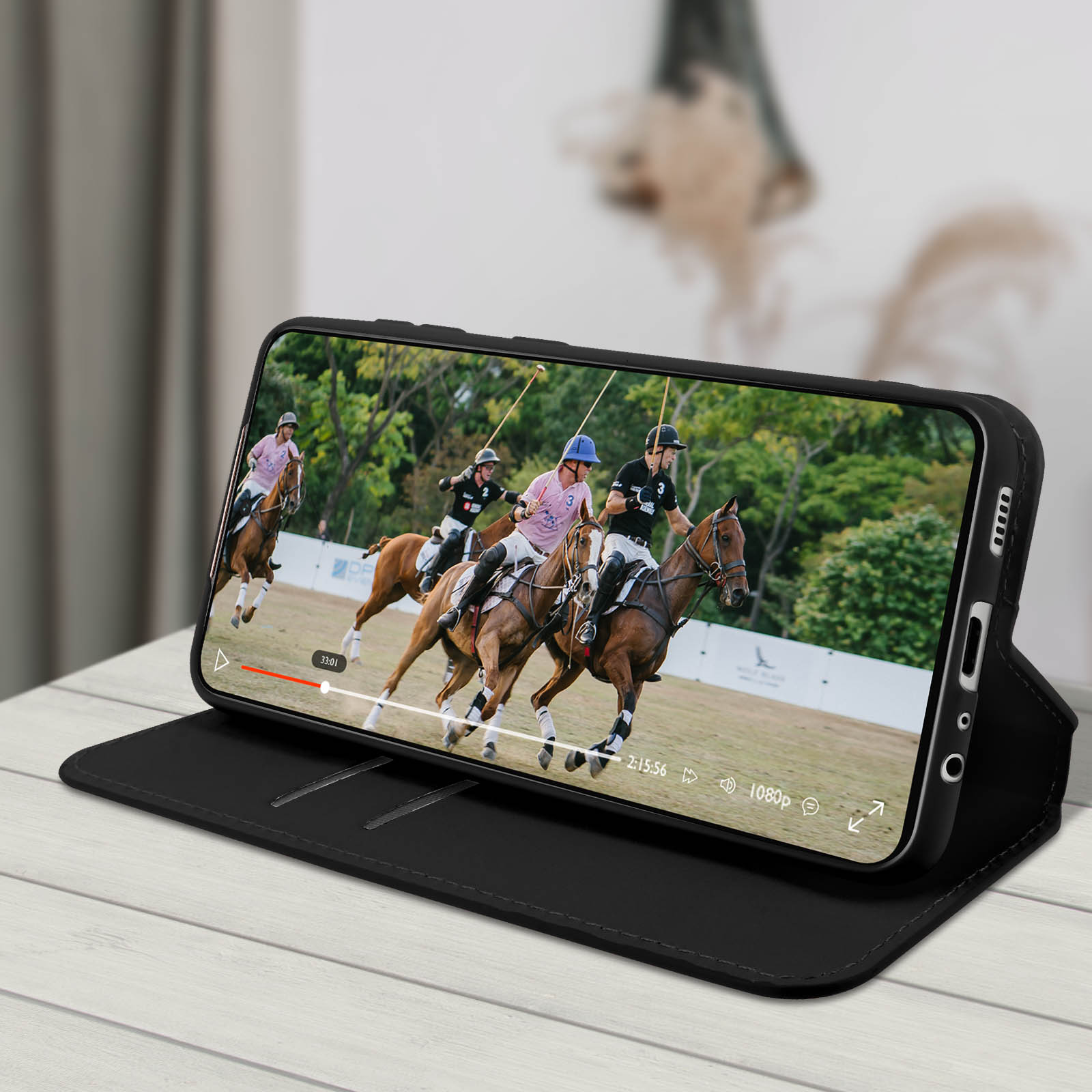 Un telefono mostra un video di una partita di polo. Il telefono è in una custodia nera, aperto su una superficie di legno.
