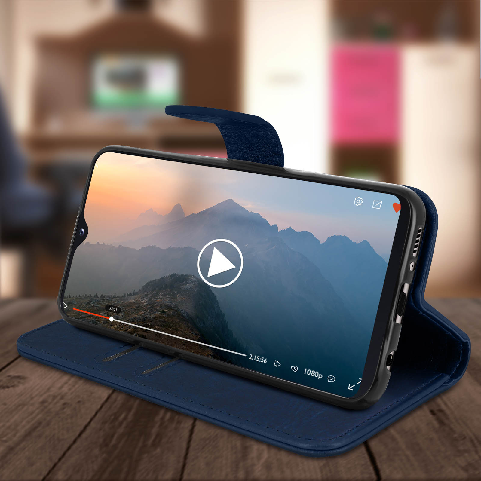 Étui de téléphone bleu, ouvert, montrant un téléphone. Sur l'écran du téléphone, une vidéo est en cours de lecture. Fond de table en bois.