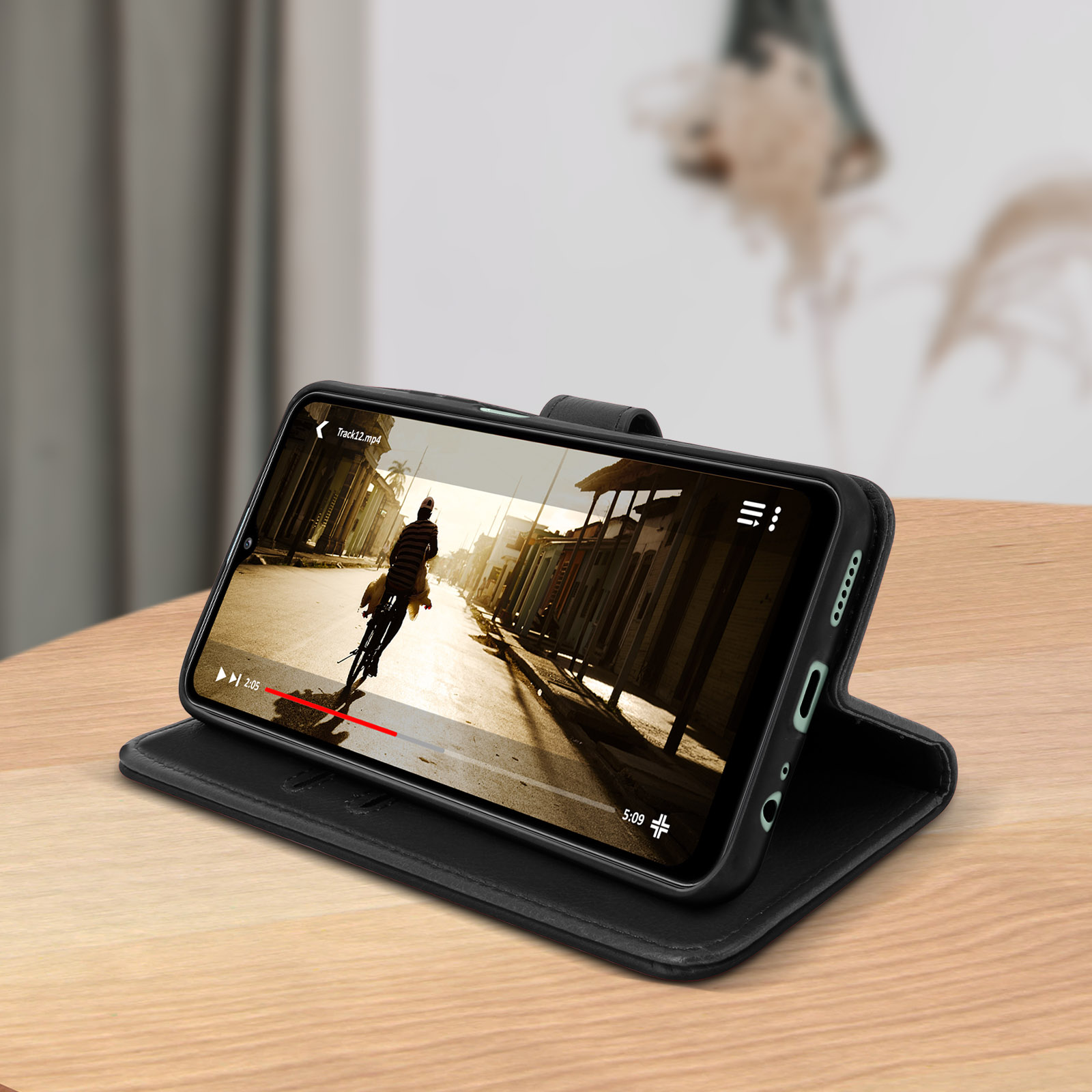 Téléphone dans un étui noir affichant une vidéo. L'étui est sur une table en bois. L'arrière-plan est flou.