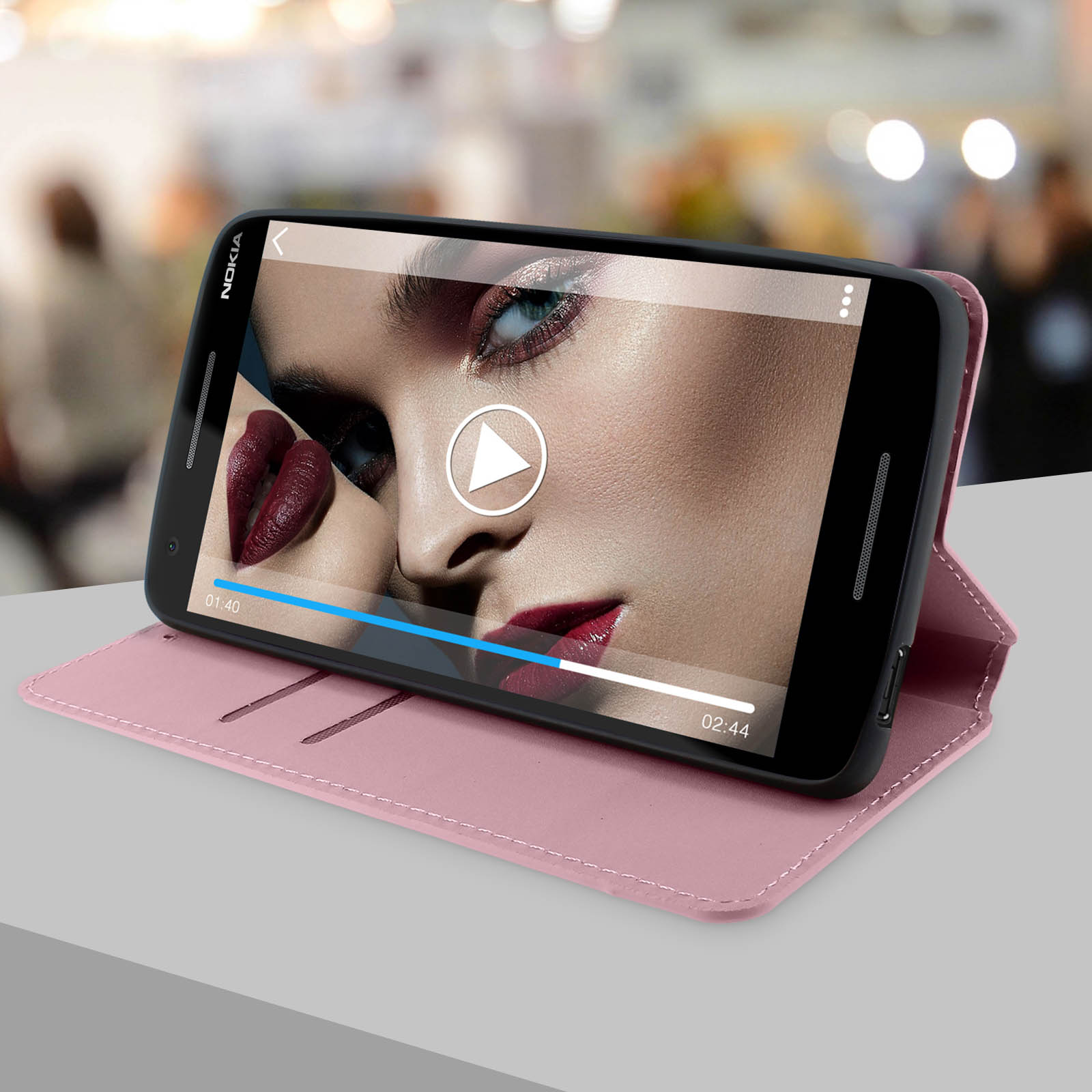 Un telefono che mostra un video con il volto di una donna. Il telefono è in una custodia rosa su una superficie grigia.