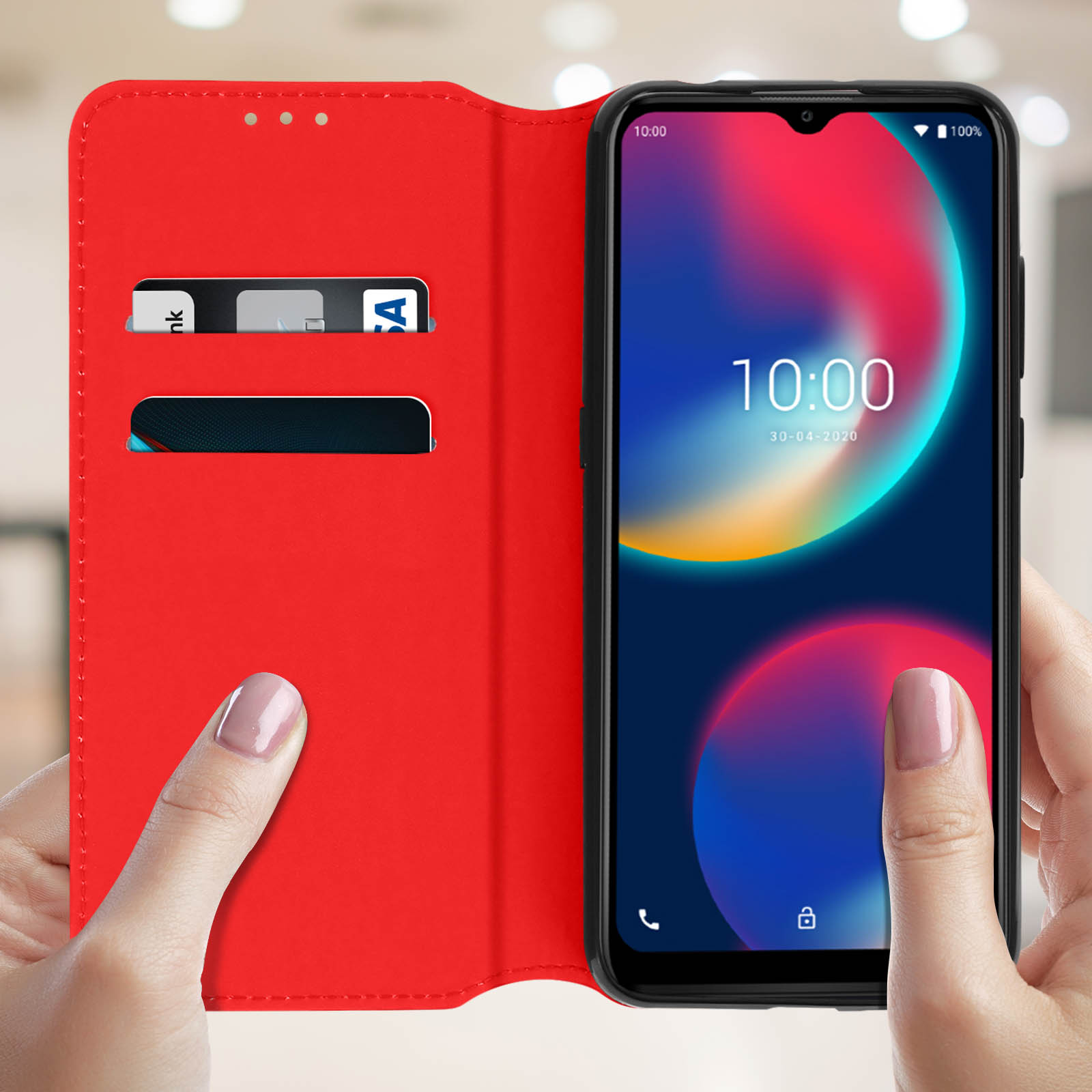 Un telefono in una custodia rossa tenuto da mani. Il telefono mostra ora, data e icone. Fessure per carte visibili.