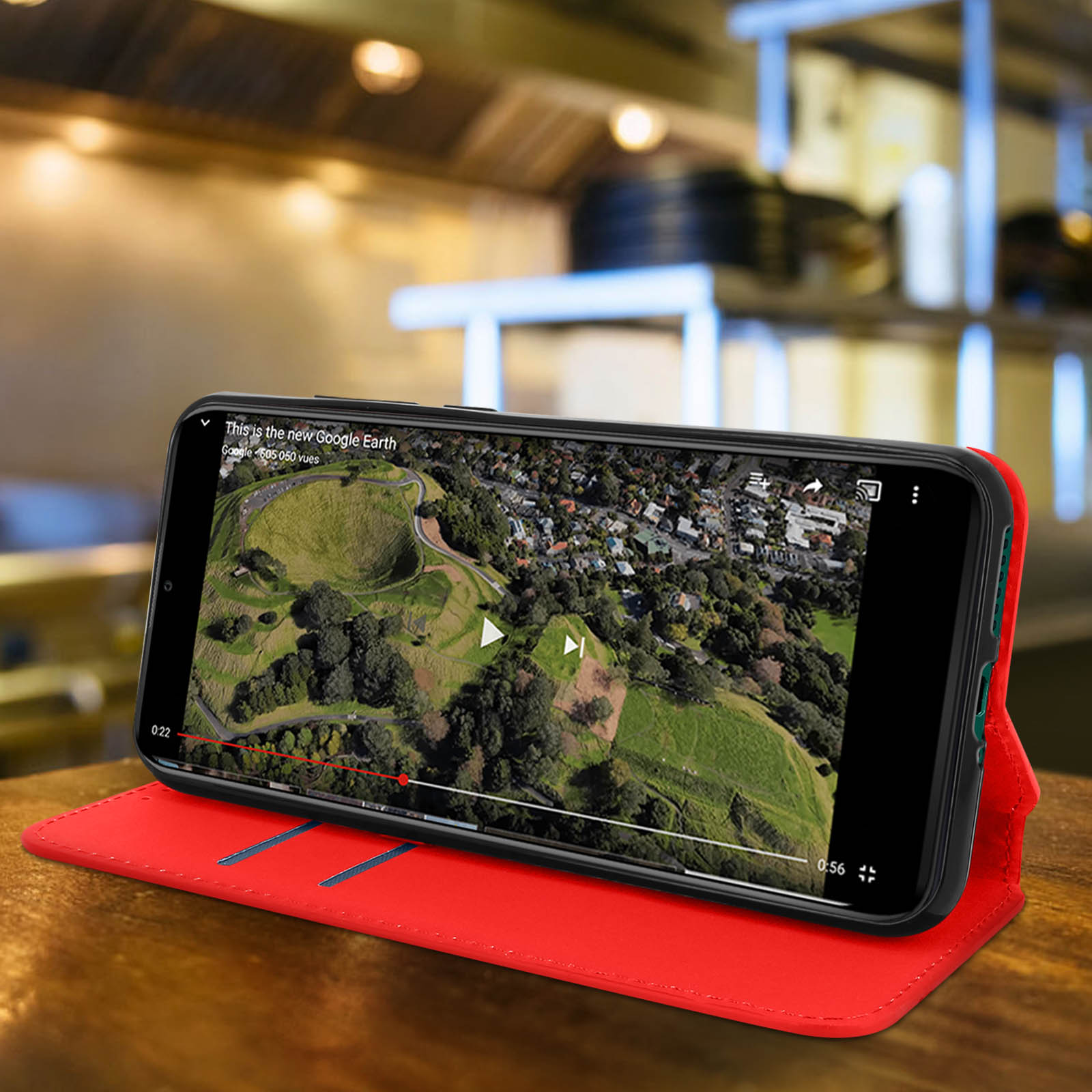 Telefono in custodia rossa, riproduce video. Tavolo in legno, sfondo del ristorante sfocato.