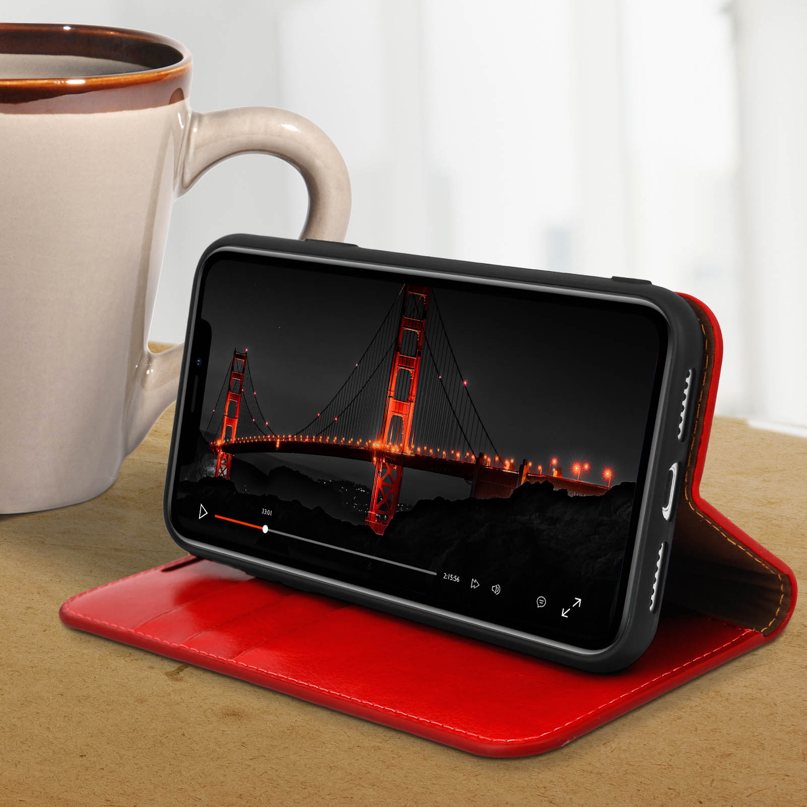 Telefono in custodia rossa mostra un video del Golden Gate Bridge di notte. Una tazza bianca sullo sfondo.