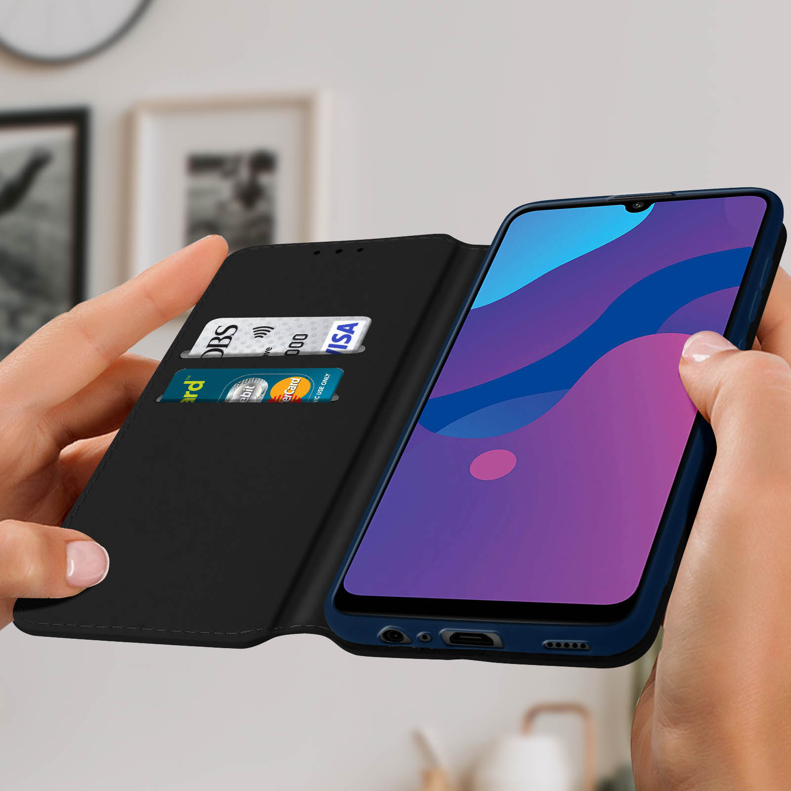 Funda negra, abierta, con un teléfono, tarjetas visibles, sujetada por dos manos.