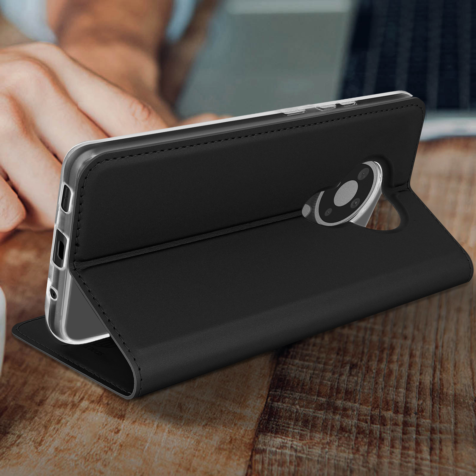 Custodia per telefono nera aperta, con un telefono all'interno, su un tavolo di legno. Una mano è vicina.